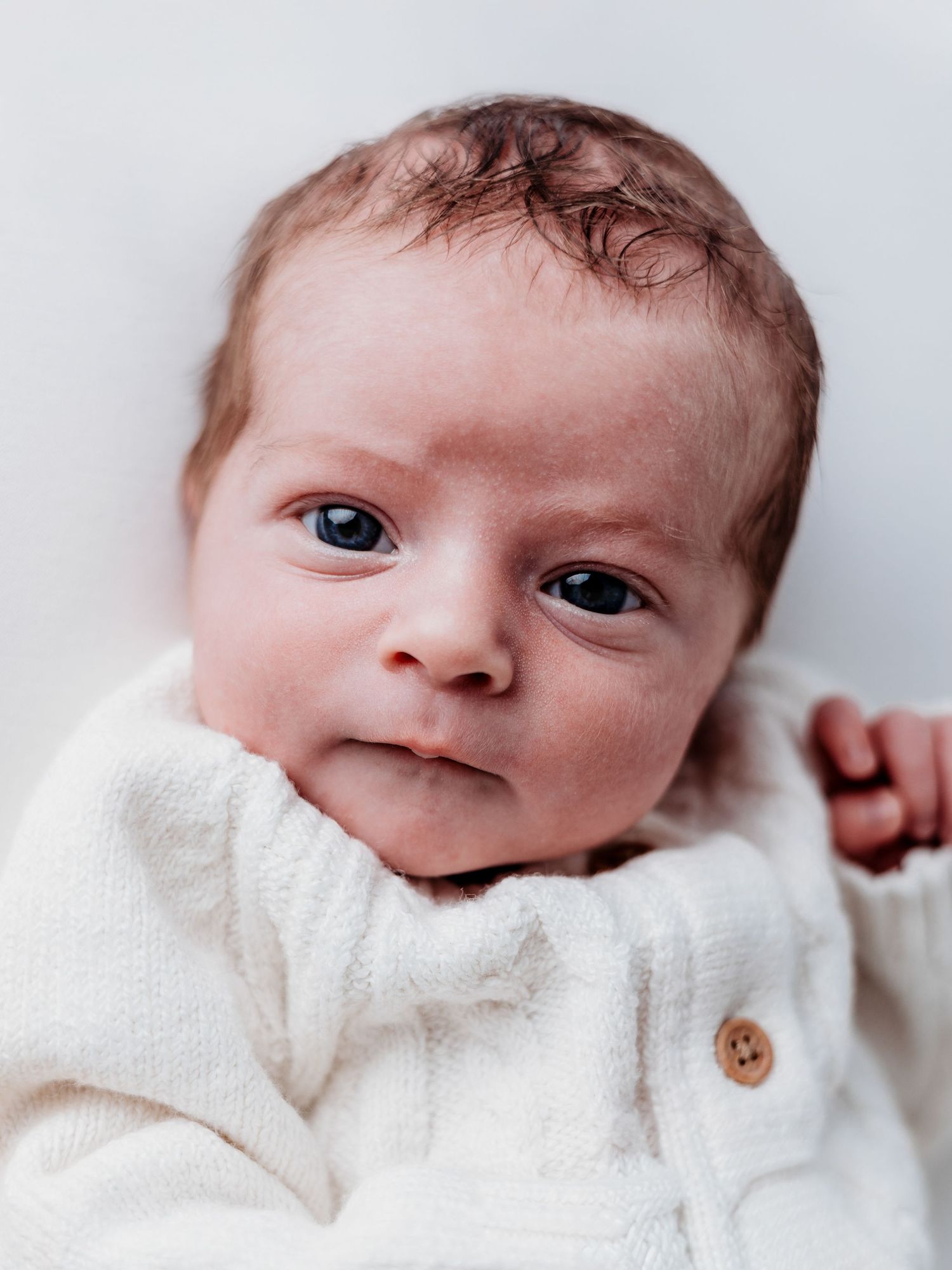 A newborn baby in a white onesie winks at the camera in a series of four connected photos.