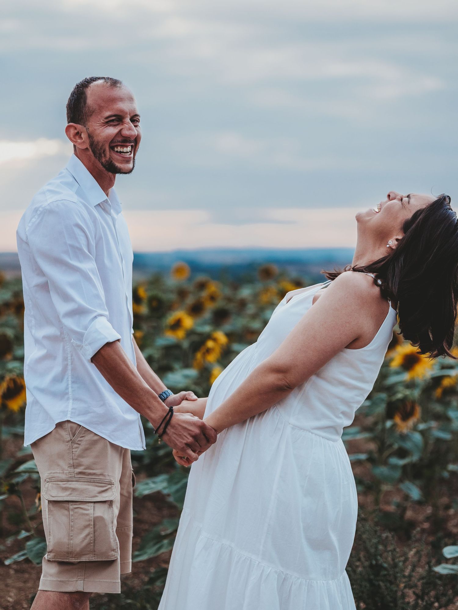 A couple shares a tender moment in a sunflower field during sunset, creating a romantic and joyful atmosphere.