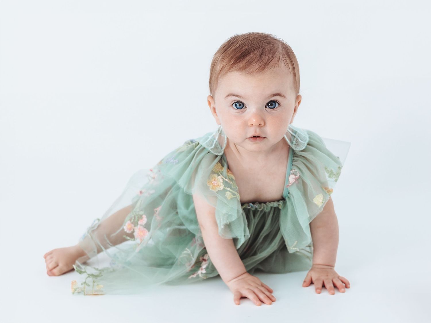 A baby wearing a mint green tulle dress crawls and poses on a white background in a series of photos.