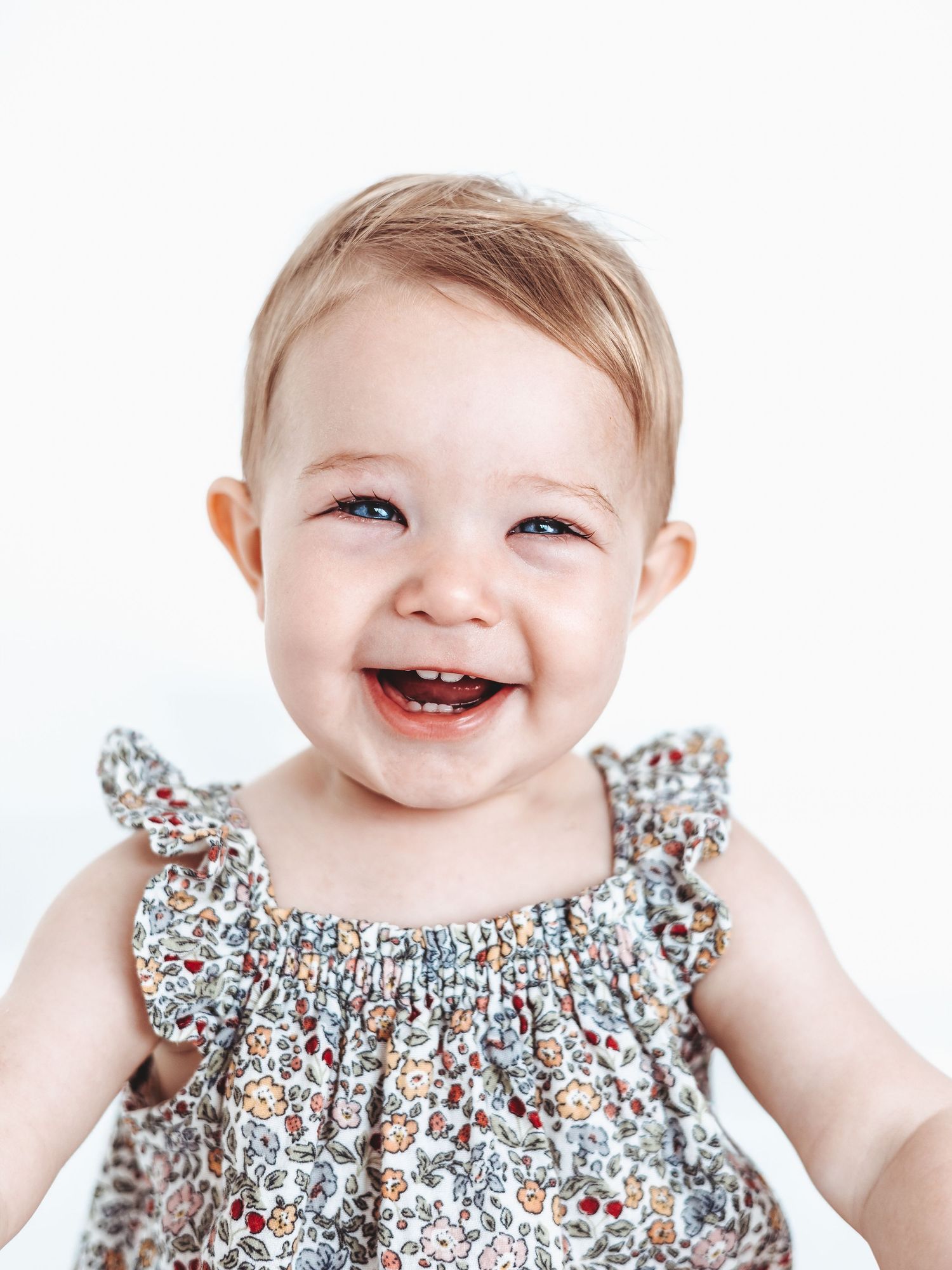 Baby wearing floral print dress smiling brightly against white background. Dorset Baby and Family Photoshoot. Poole and Bournemouth.
