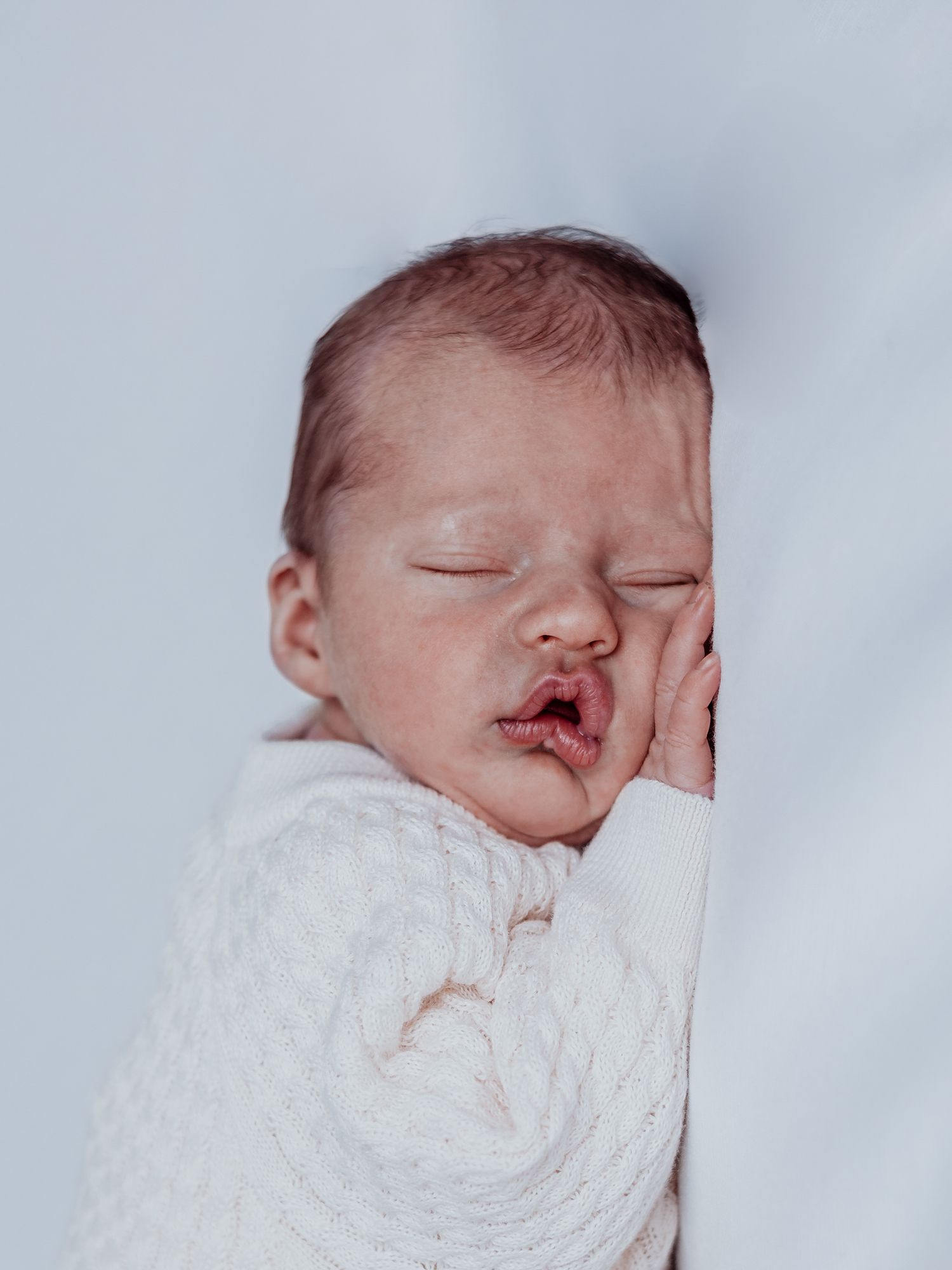 A sleeping newborn baby swaddled in white blankets shown from different angles in a series of photos.