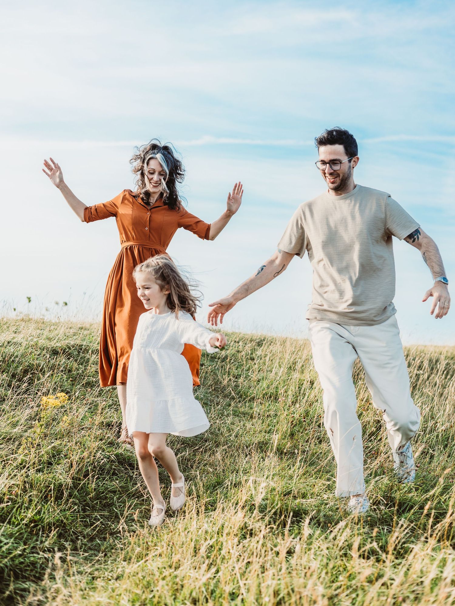 A joyful family of three playing in a sunny green meadow, with parents and daughter holding hands and dancing.