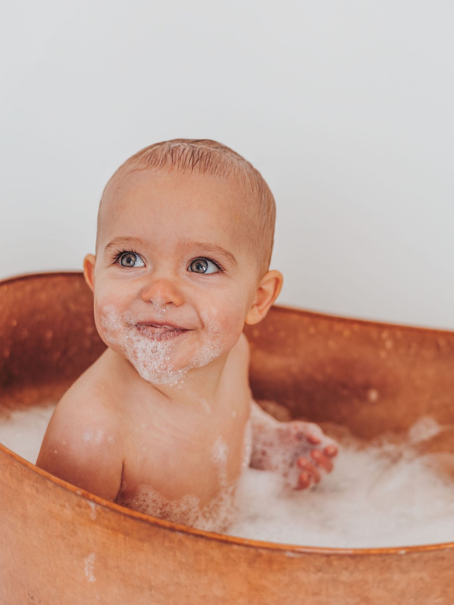 A baby with flour-covered face peers out from a wooden bowl during messy sensory play.