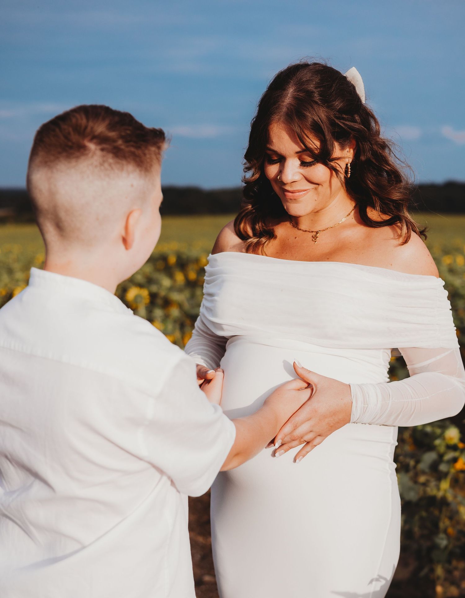 A couple in white outfits embracing in a sunlit field of sunflowers during a romantic photoshoot.