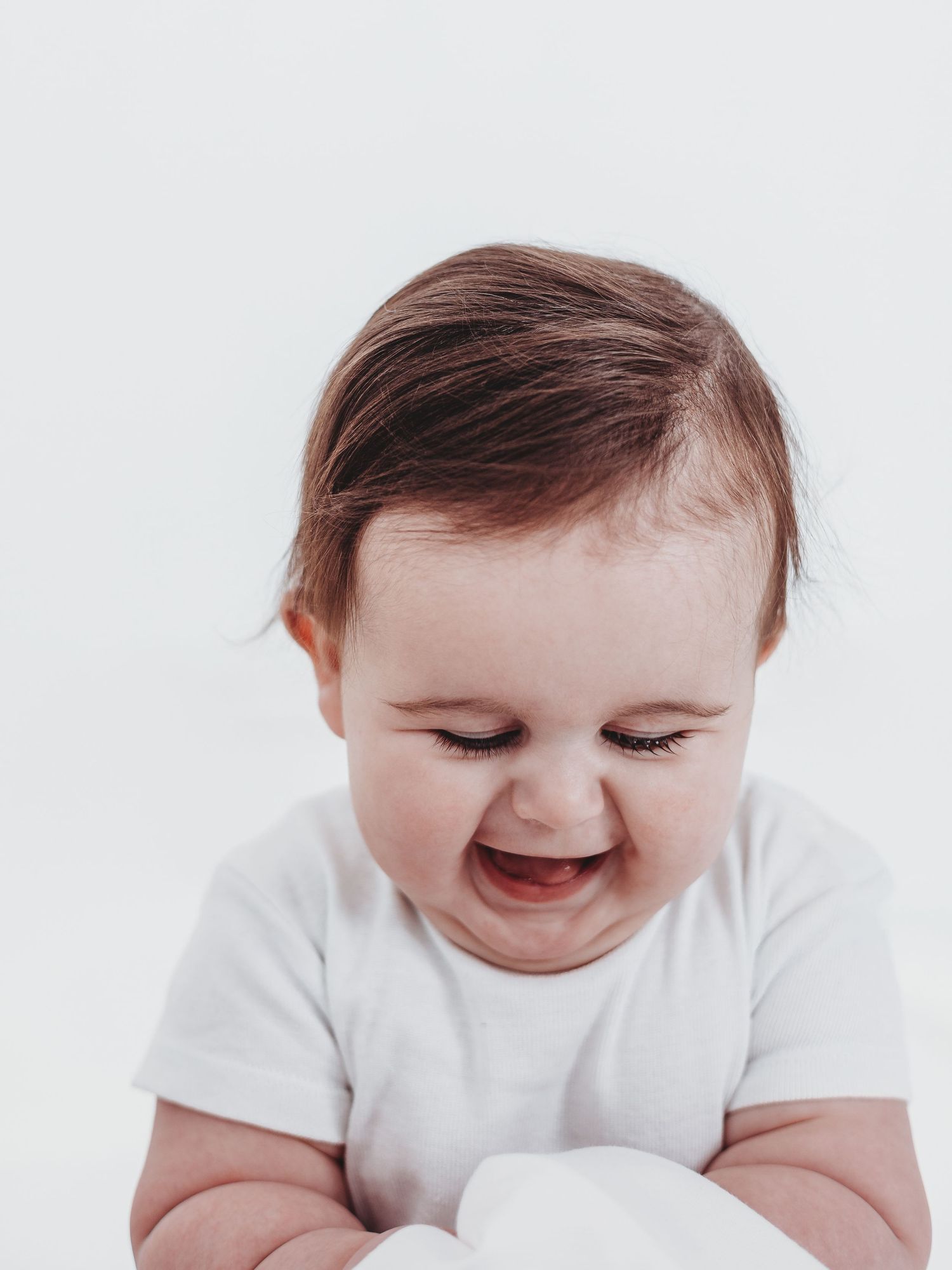 A baby in a white onesie smiles and looks down while lying on a white background in a series of connected photos.