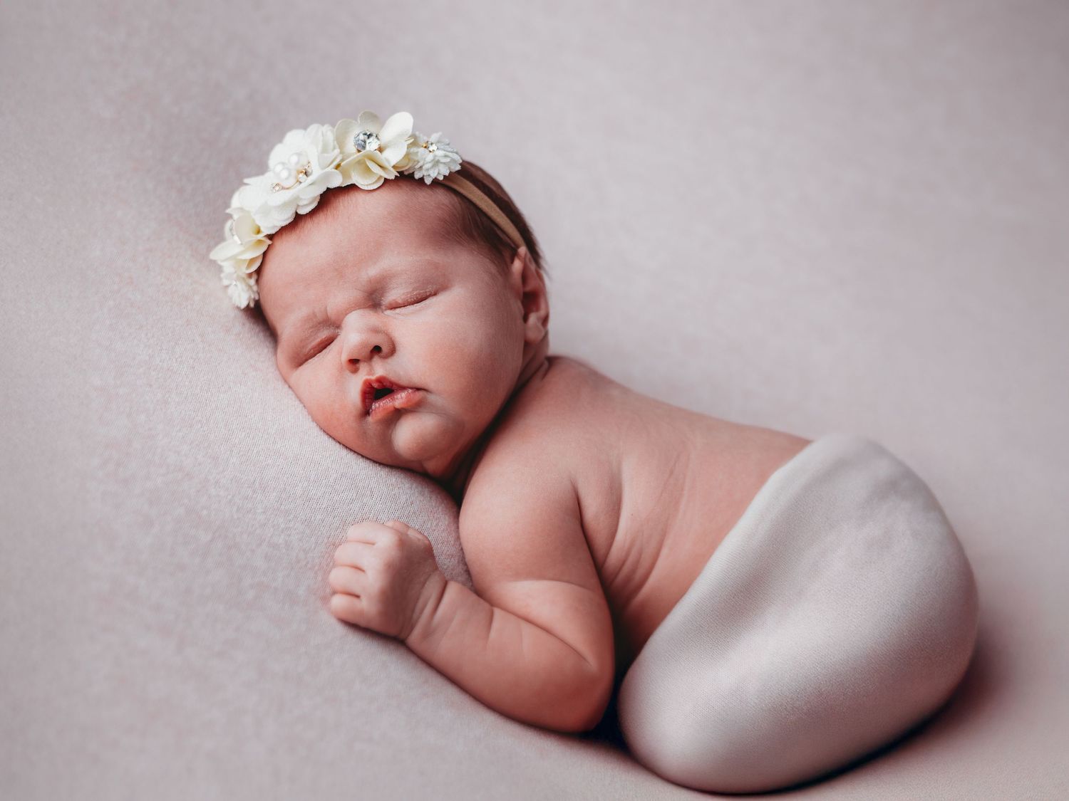 A sleeping newborn baby lies peacefully in soft gray and white tones during a professional photo session.