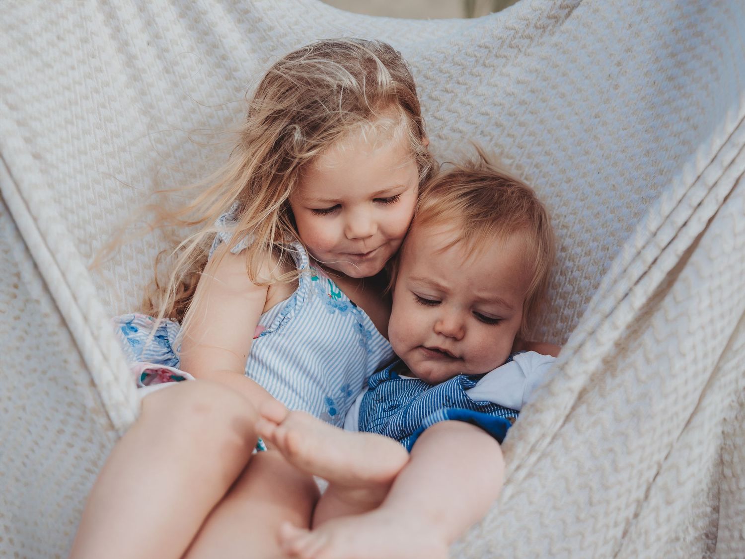 A mother and child share a tender moment while resting together on a cozy hammock in soft lighting.