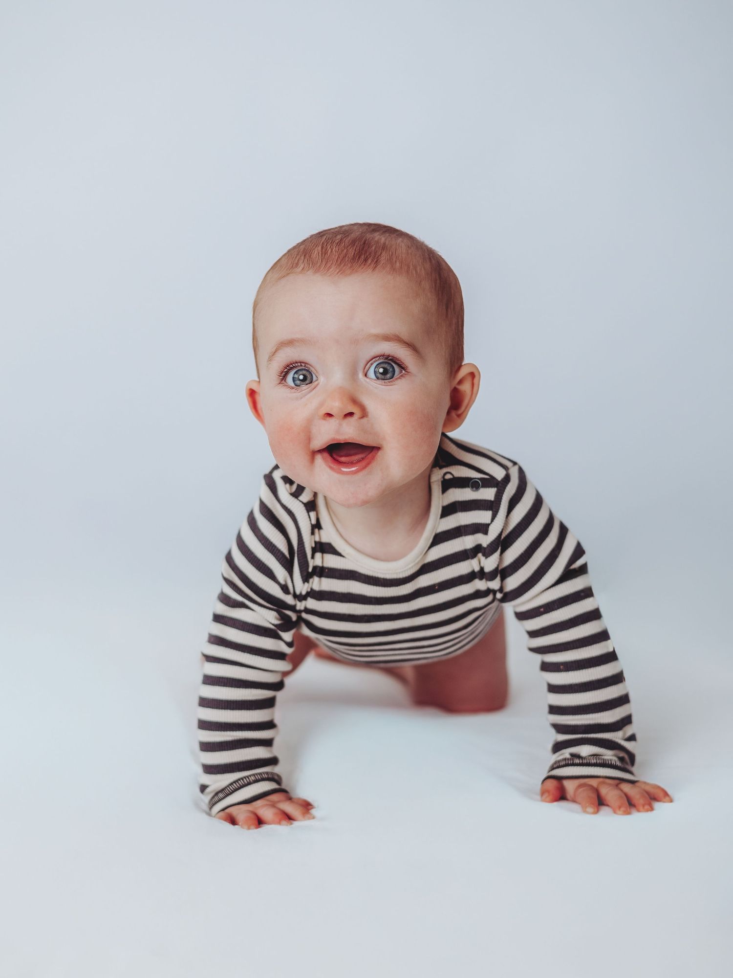 A baby wearing a black and white striped shirt crawls and plays on a white background in a photo series.
