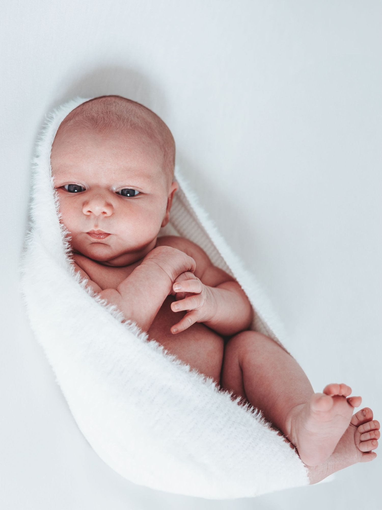 Newborn baby wrapped in soft white blanket against light background. Dorset Newborn Photoshoot. Poole and Bournemouth.
