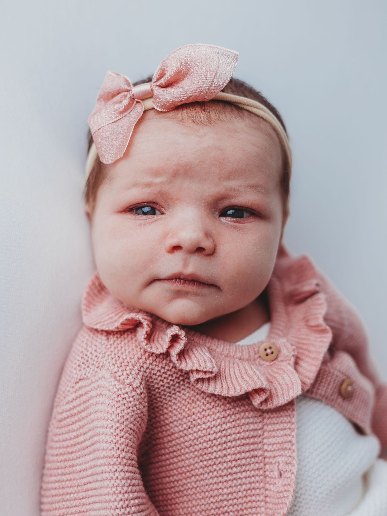 A newborn baby wearing a soft pink knitted sweater and matching bow headband in a series of close-up portraits.