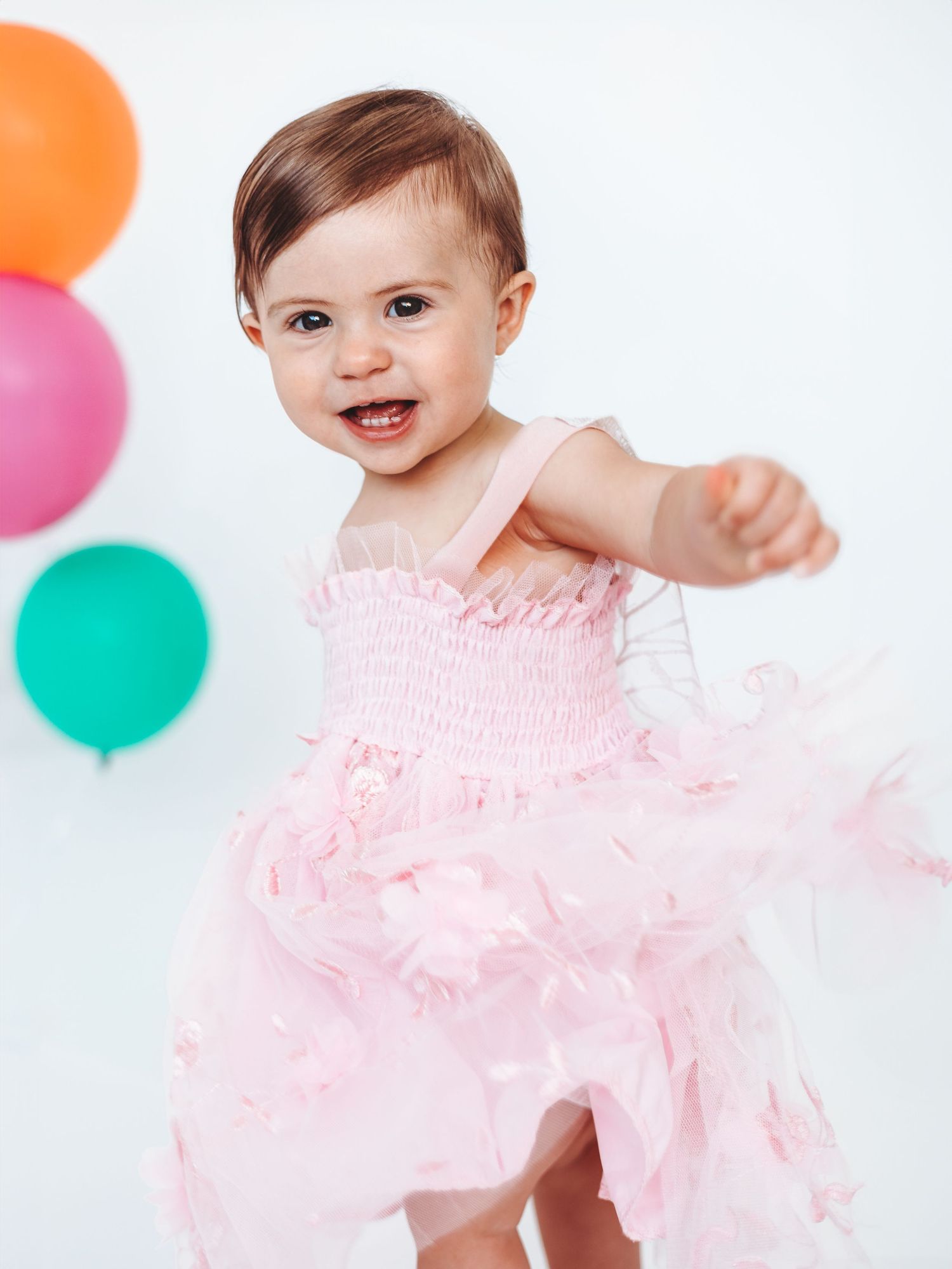 Baby in pink tulle dress dancing with colourful balloons in the background. Dorset Baby and Family Photoshoot. Poole and Bournemouth.