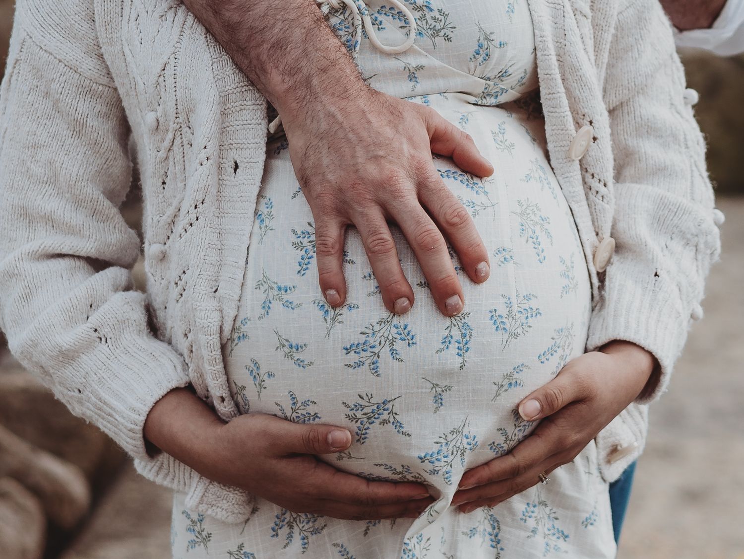 Close-up of hands cradling a pregnant belly wearing a delicate floral dress during a maternity photoshoot.