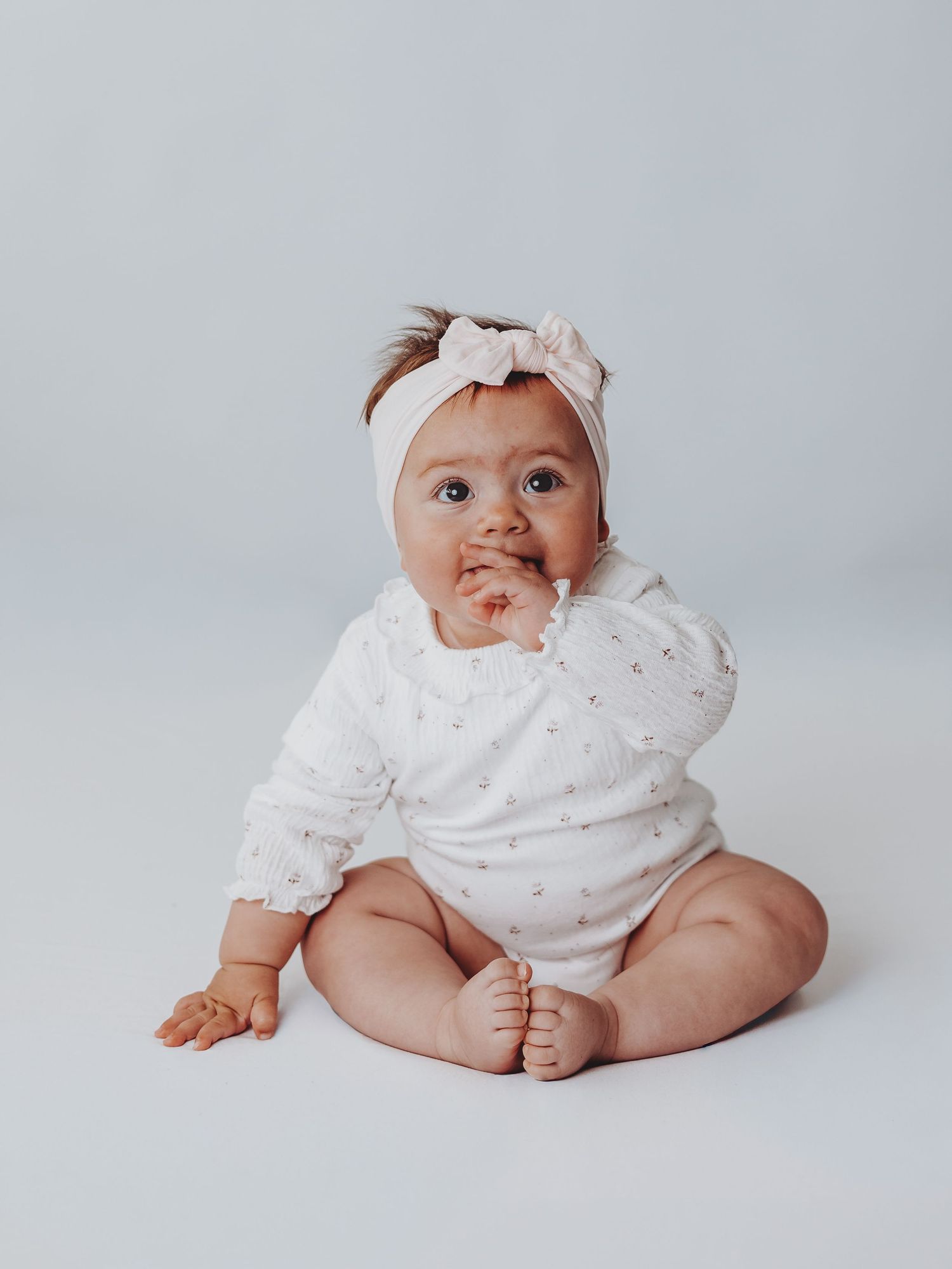 A baby in white polka dot clothing poses in various positions on a light gray backdrop during a photo shoot.