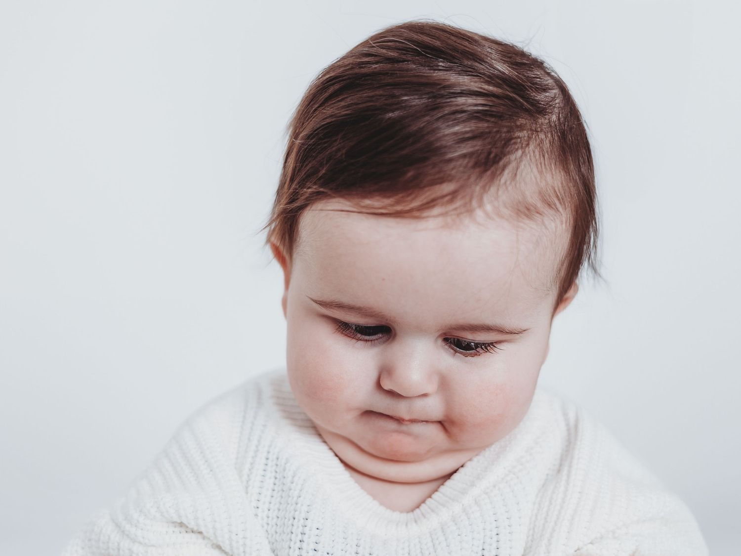 A baby in a white sweater shows four different facial expressions in a photo collage.