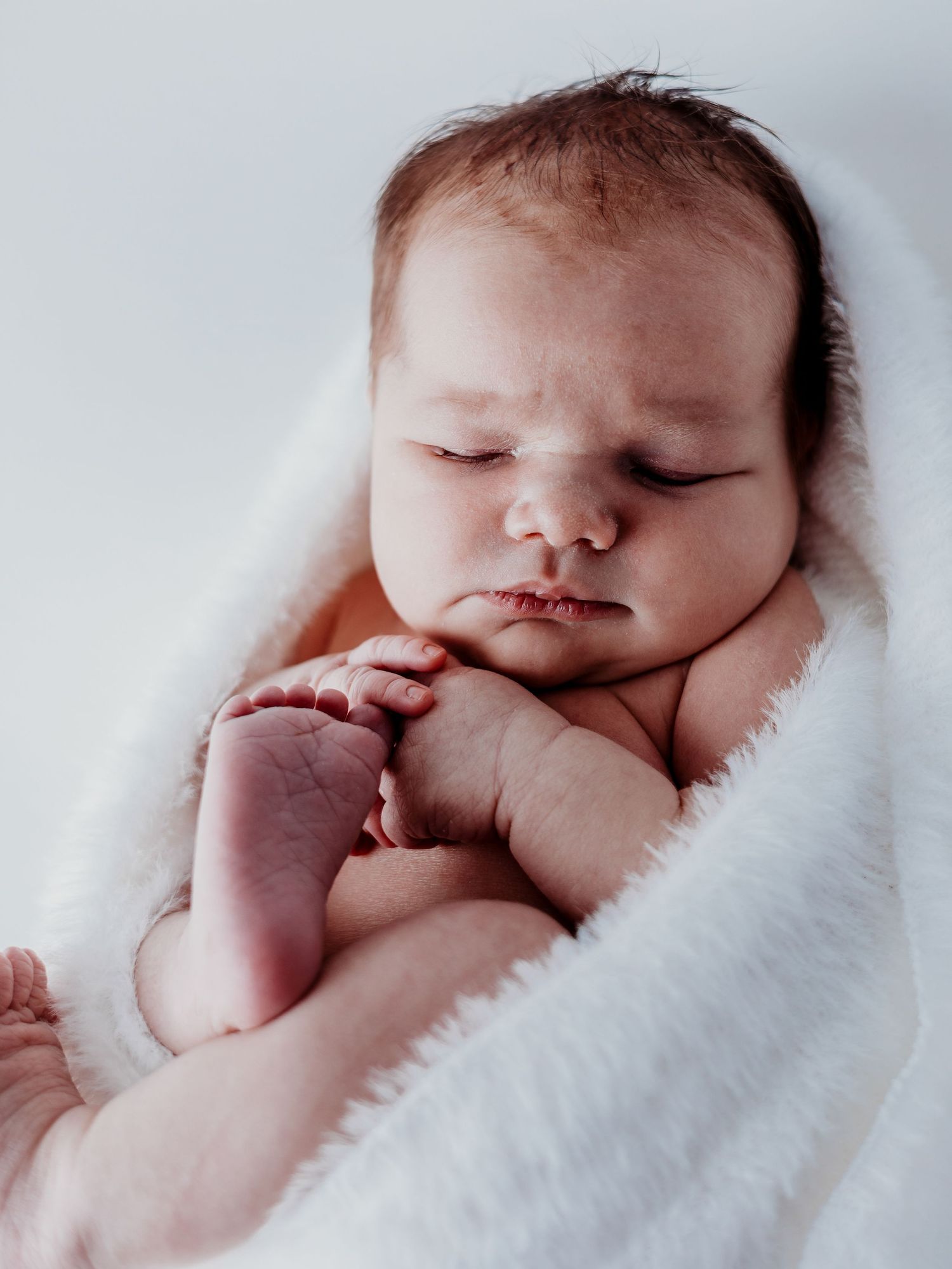 Sleeping newborn baby wrapped in white blanket shown in three peaceful closeup poses.