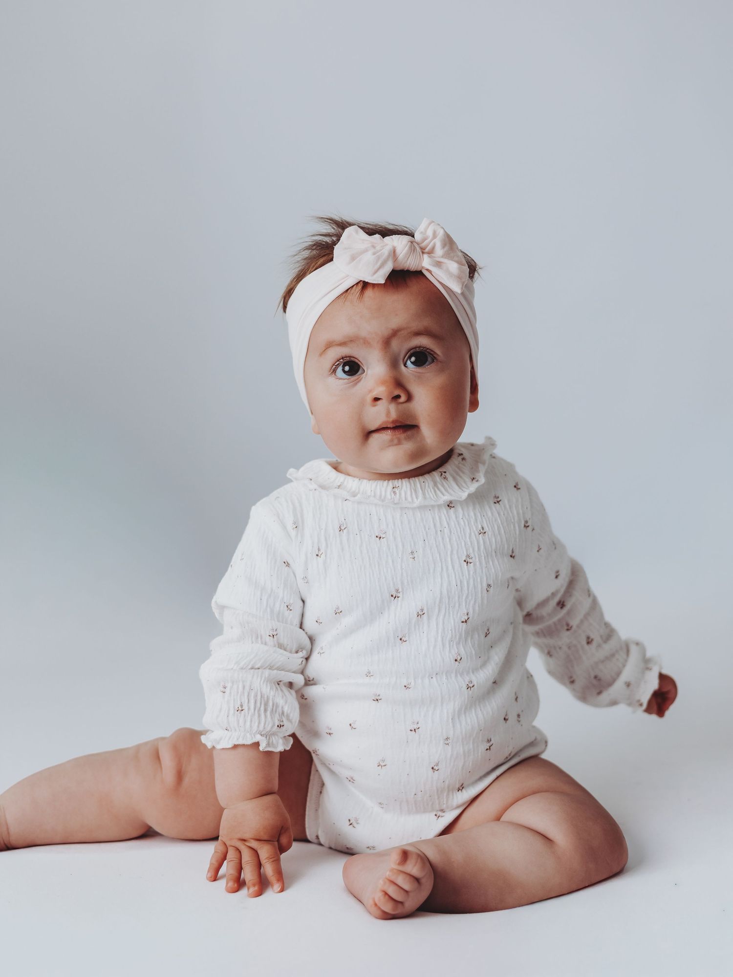 Baby wearing white knit outfit and bow headband sitting on white backdrop in different positions.