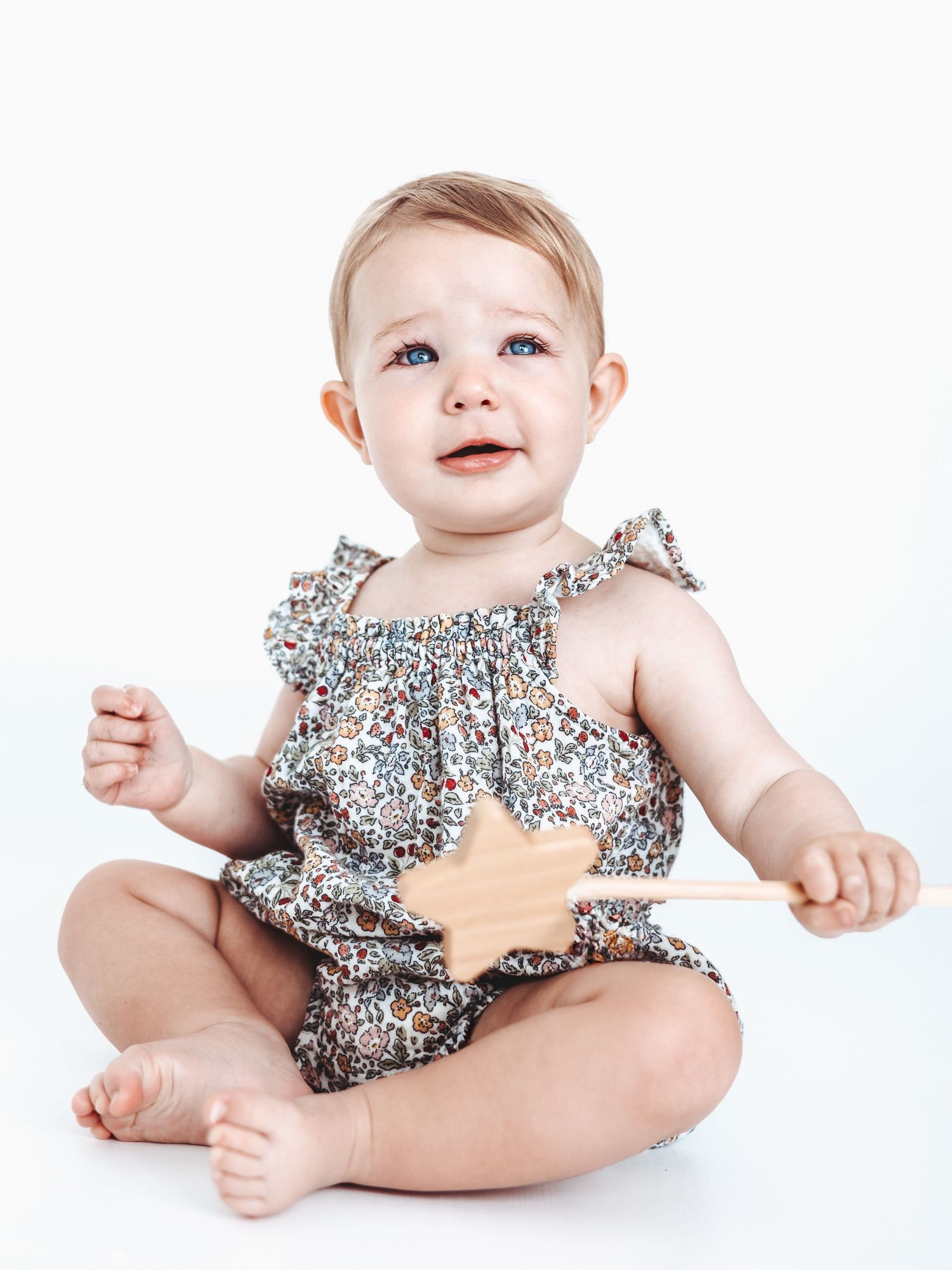 Baby wearing floral print ruffle romper sitting on white background.