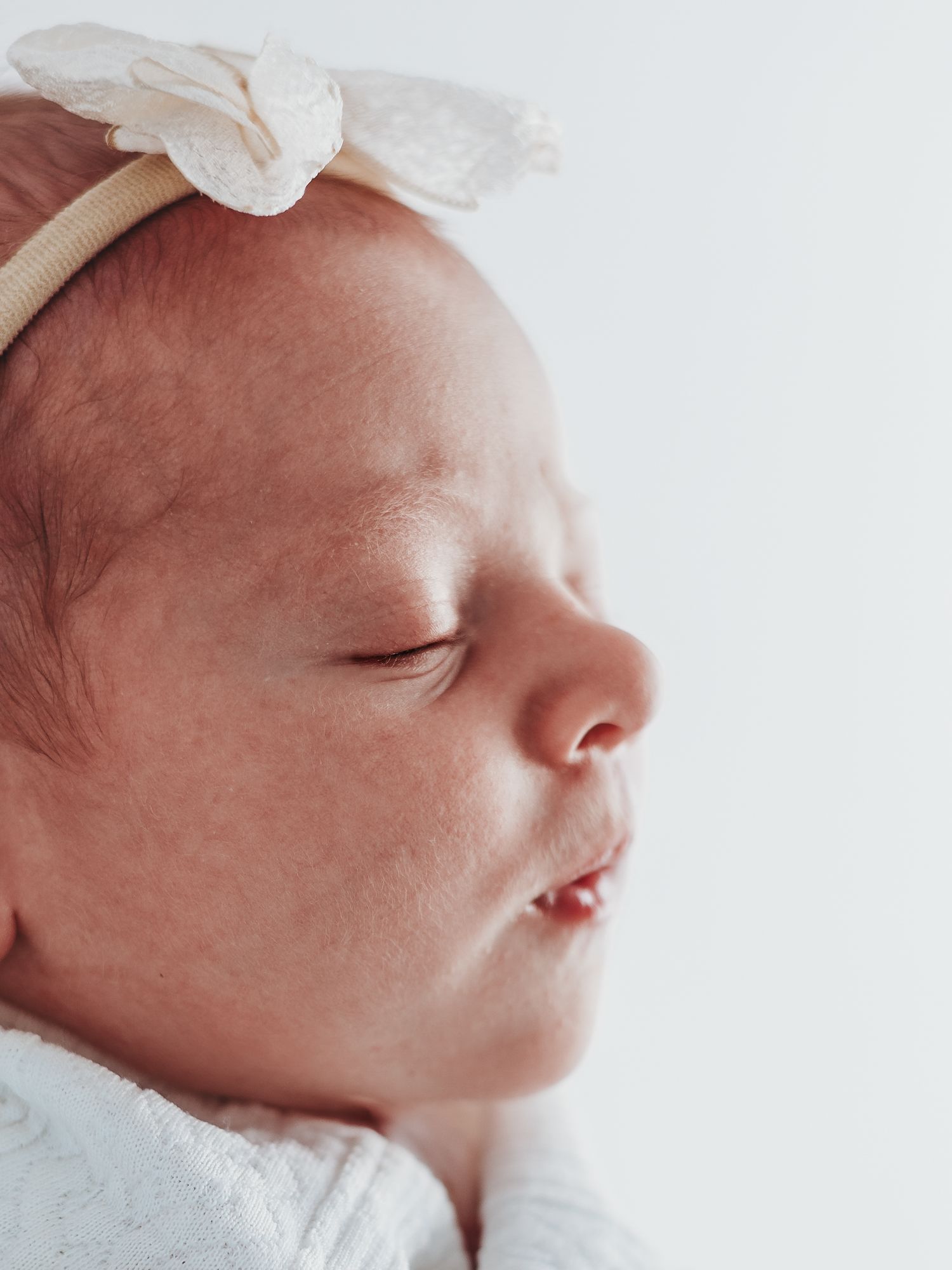 Close-up profile view of a sleeping newborn baby with delicate features against a light background.