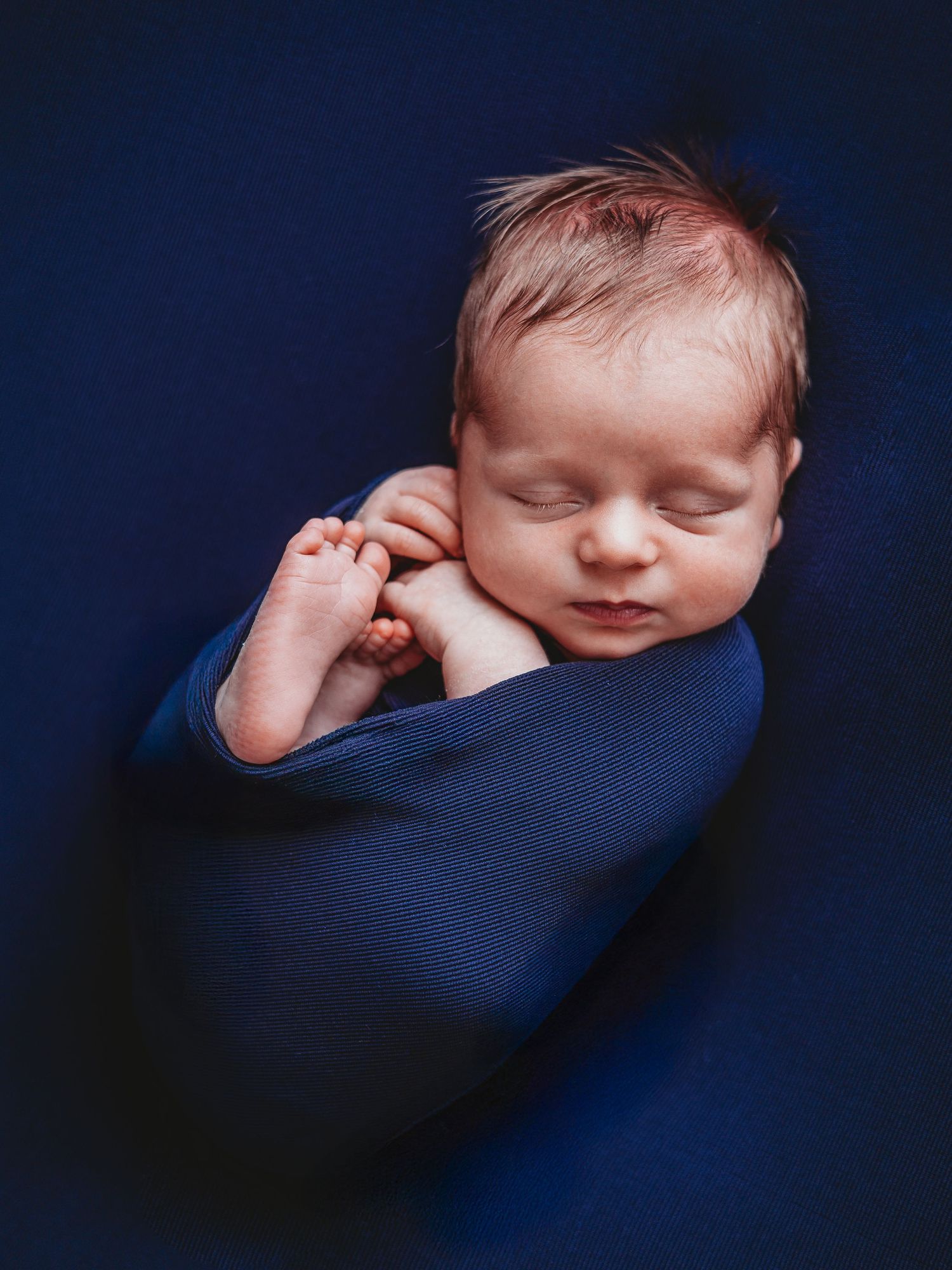 Sleeping baby in dark blue blanket shown from different angles in artistic newborn photography series.