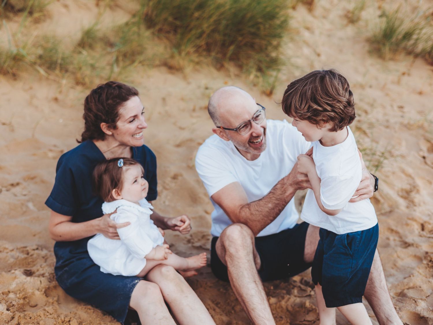 Family members sitting together and laughing on sandy beach during golden hour photography session.