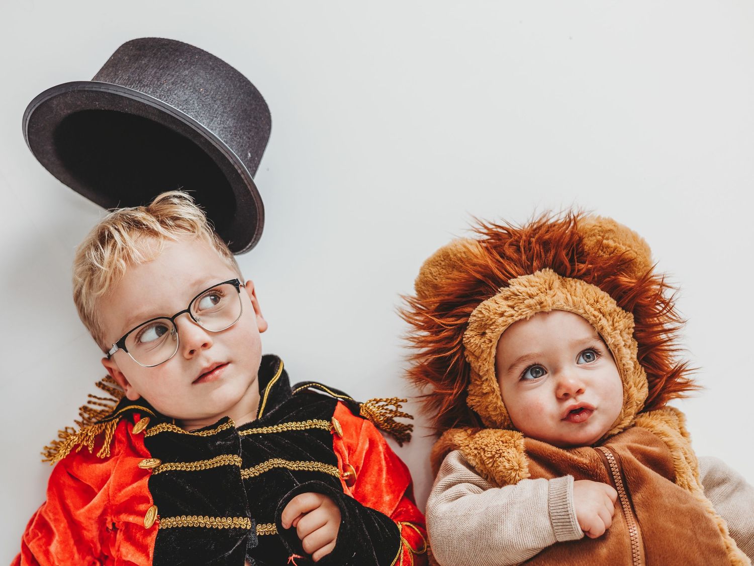 Two children in Halloween costumes, a ringmaster and a lion, posing together against a white background.