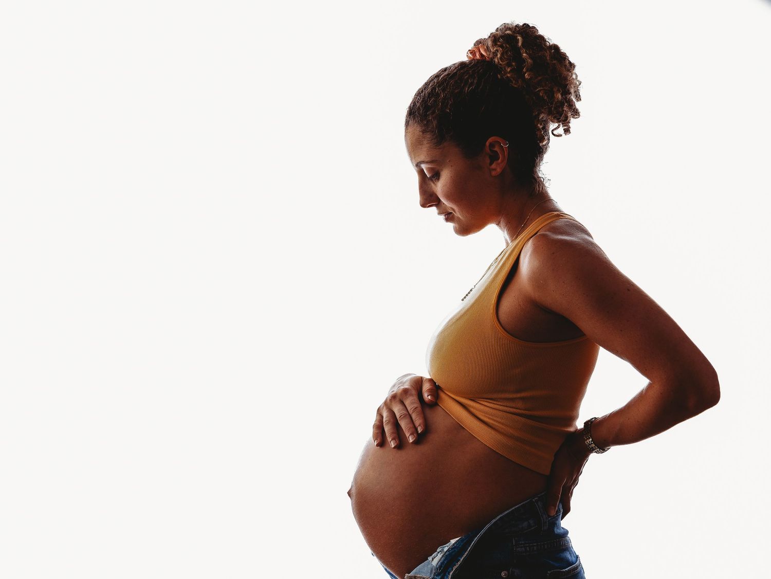 Silhouette of pregnant woman in crop top against white background showing side profile of baby bump.