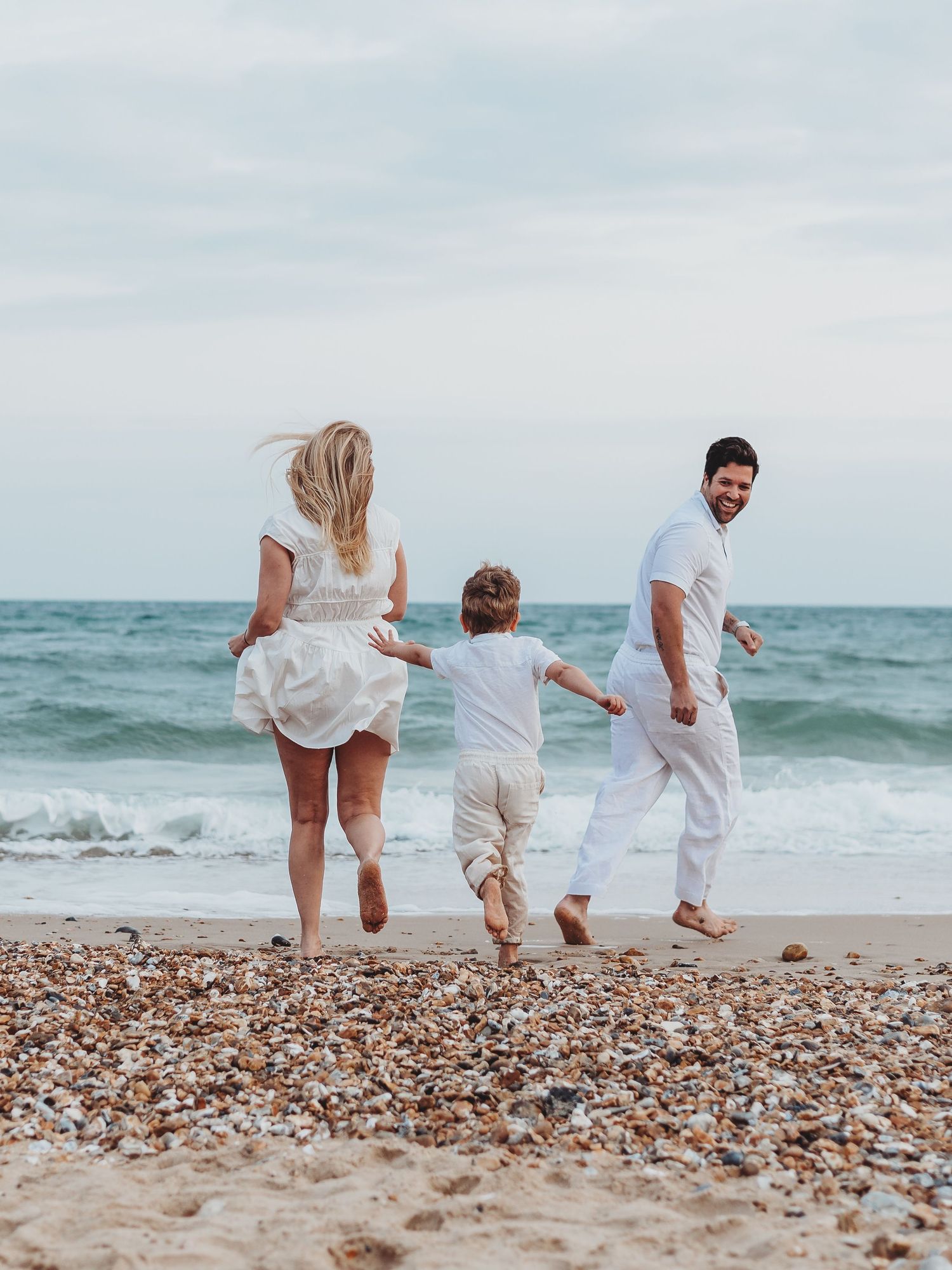 Family walking together on a pebble beach near ocean waves, shown in four progressive candid shots.