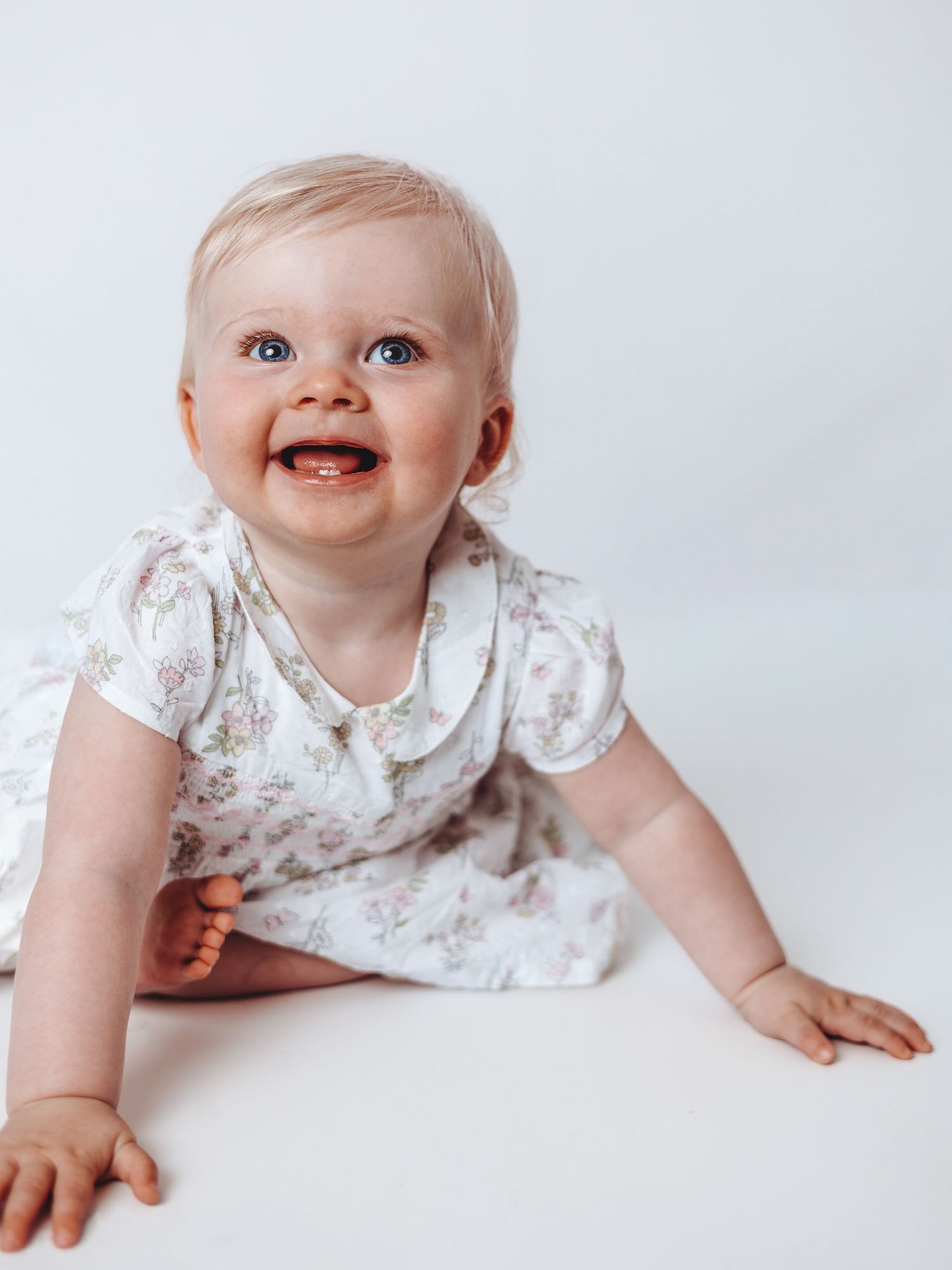 Baby wearing floral print outfit smiles and crawls on white backdrop in series of connected photos.