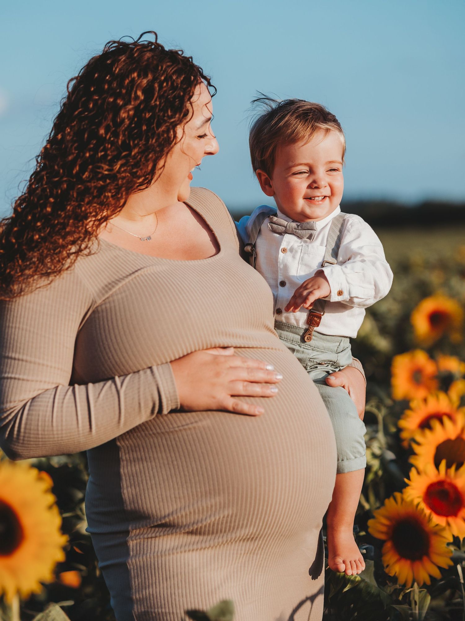 A heartwarming maternity photoshoot in a sunflower field shows tender moments between family members at sunset.