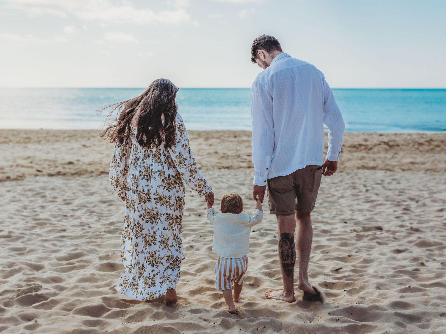 A family holding hands while walking together on a sandy beach with turquoise ocean waters in the background.