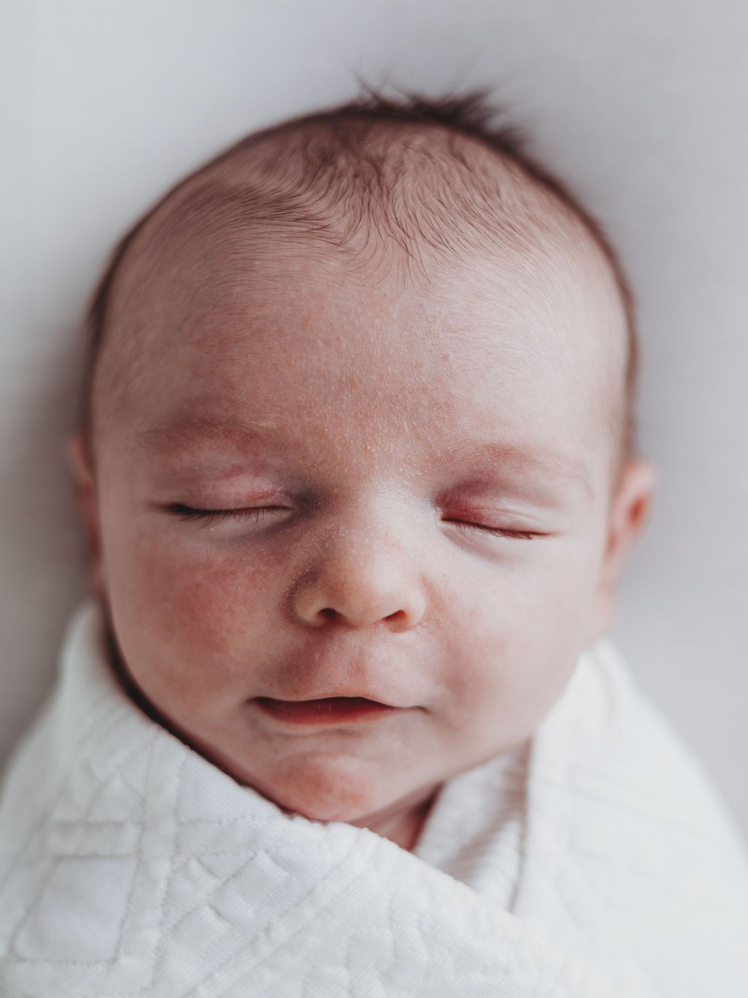 A peaceful sleeping newborn baby swaddled in a white blanket with soft lighting and delicate features.
