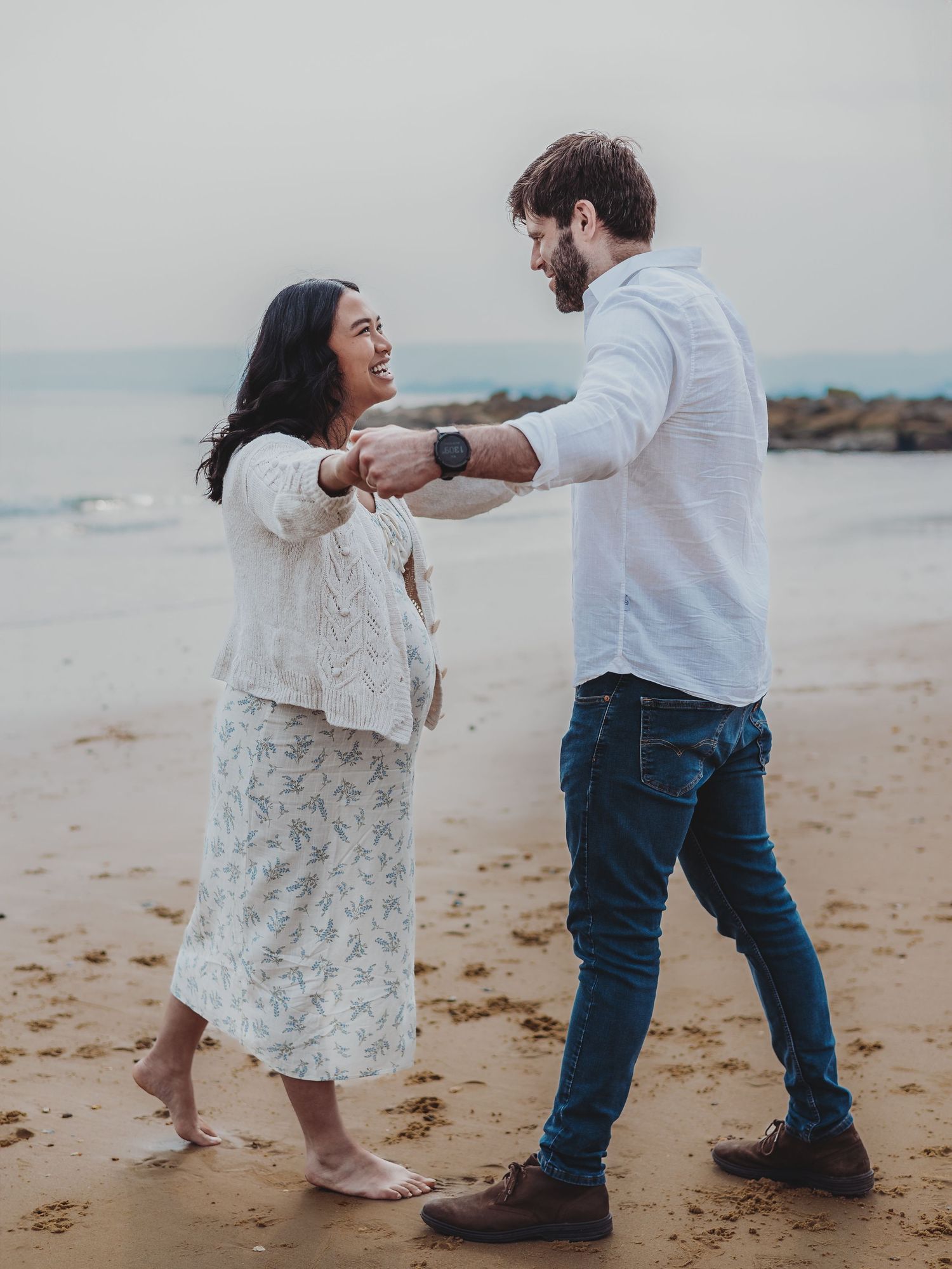 A couple shares a romantic moment dancing together on a sandy beach during a cloudy day.