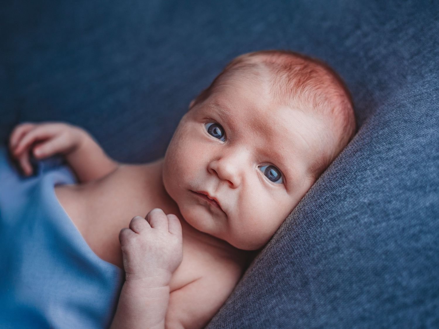 A newborn baby lies on a soft blue blanket in a series of photos showing different expressions and angles.