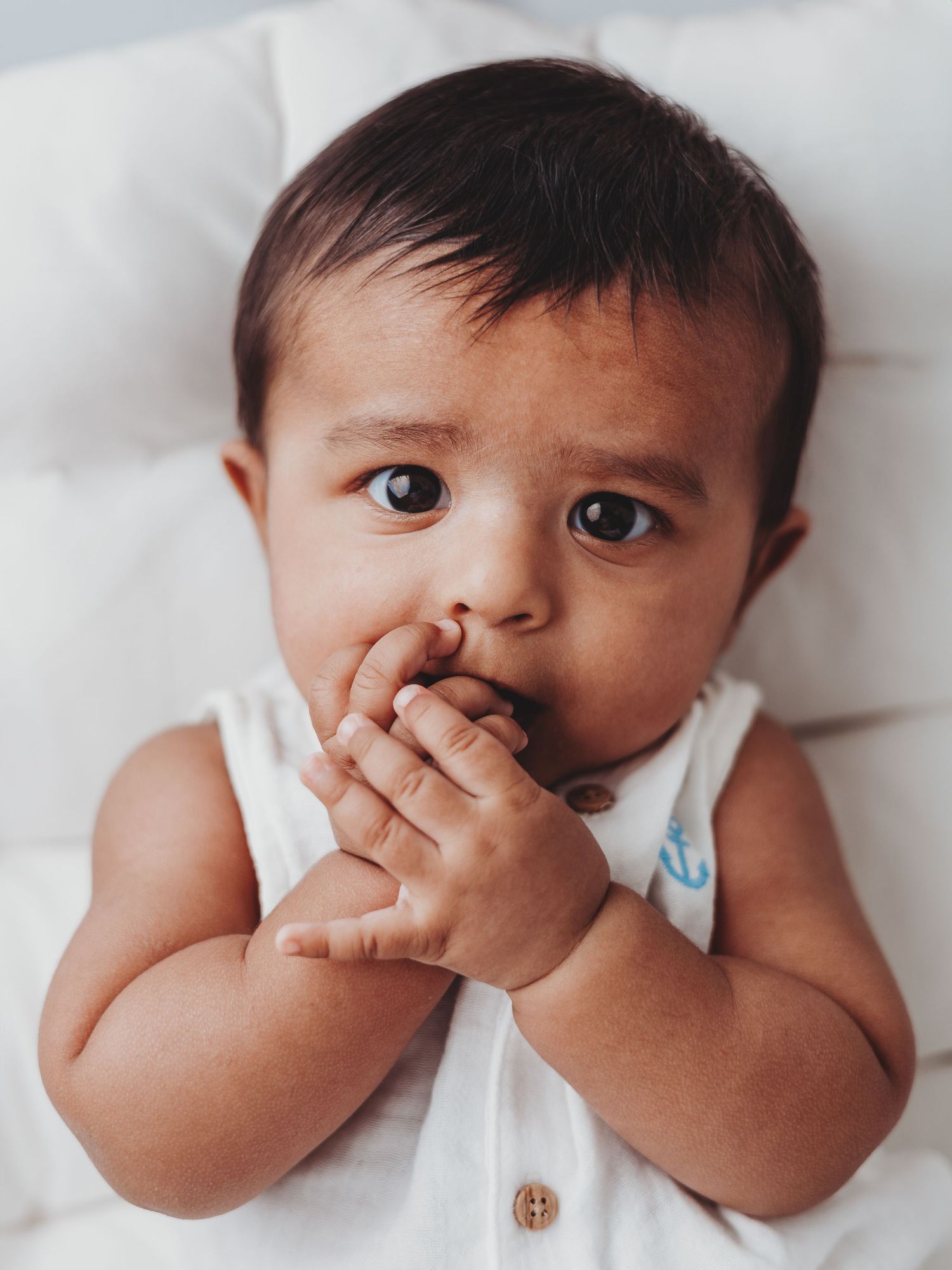 A series of photos showing a baby in white clothing touching their nose while lying on white bedding.