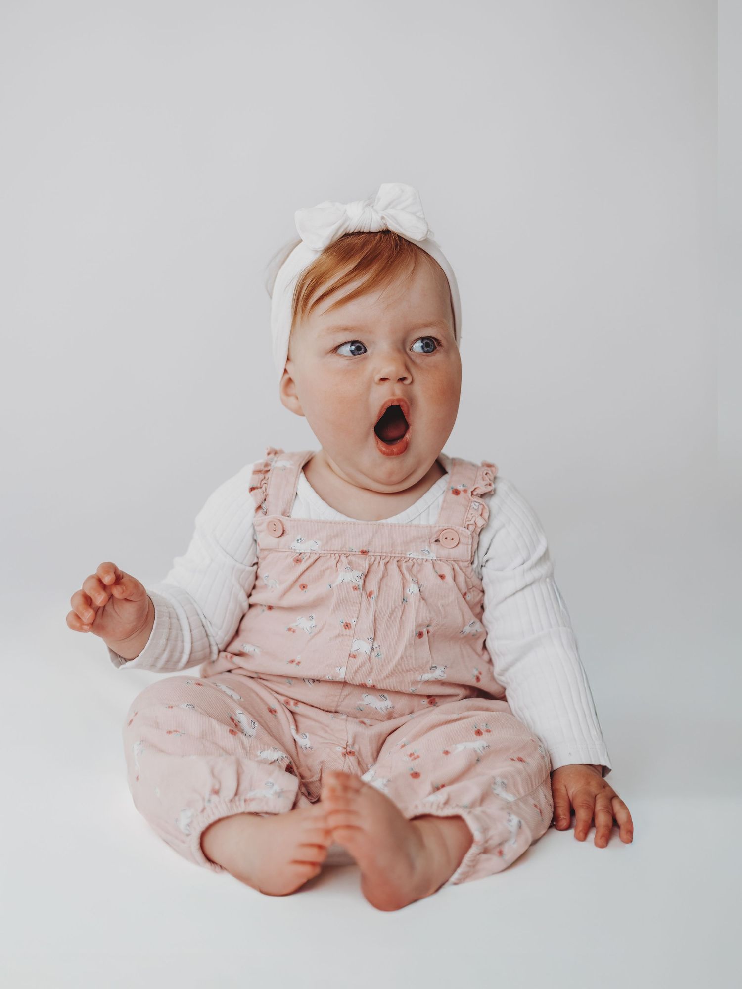 Baby in pink floral overalls and white shirt shown in four sequential poses on light background.