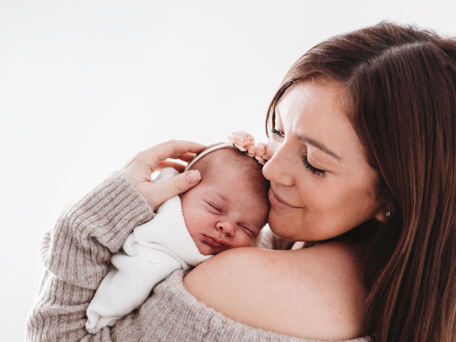 A tender moment captured between parent and newborn baby in soft, neutral tones.