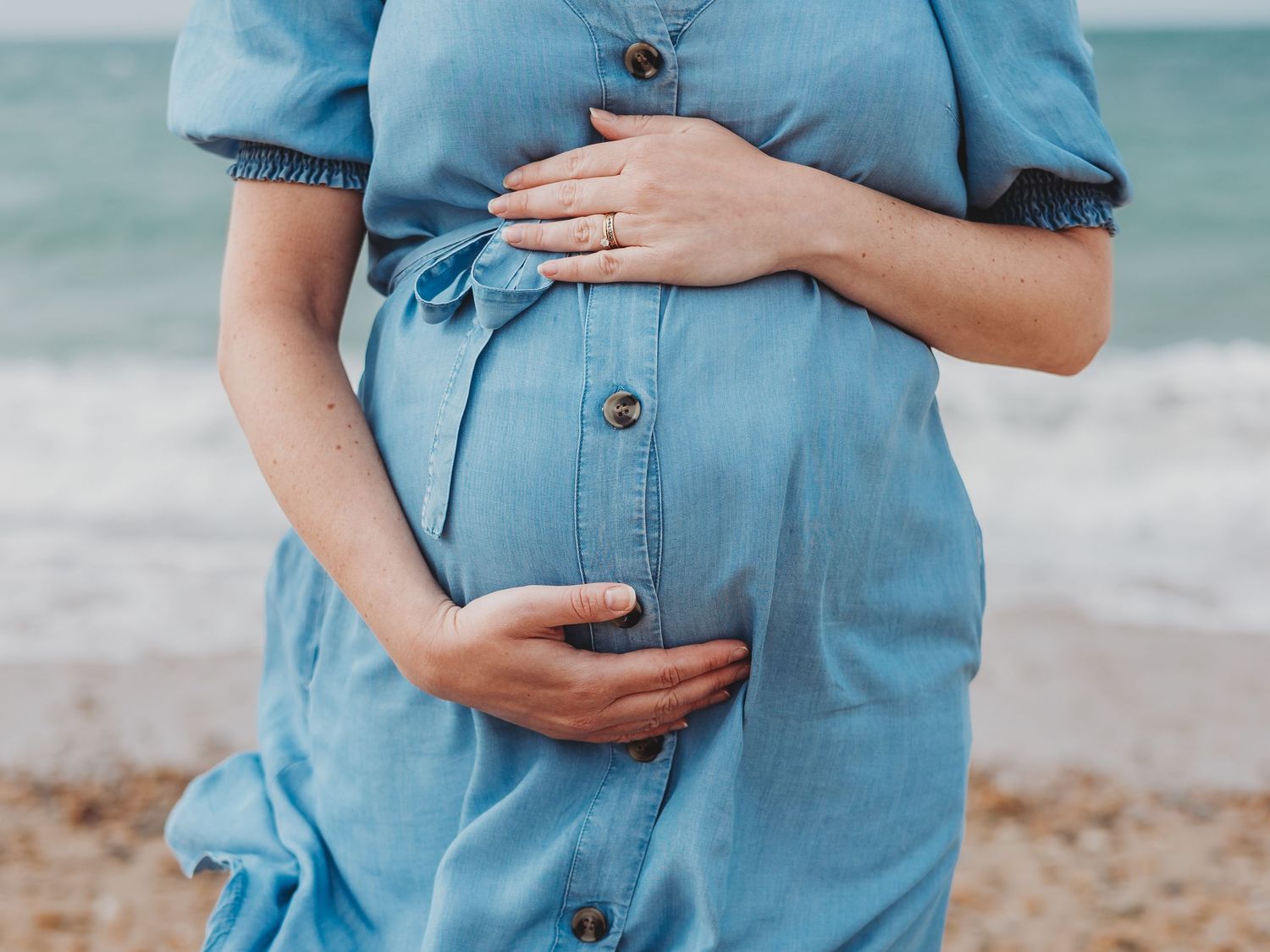 Close-up details of a light blue denim maternity dress shown in multiple angles at the beach.