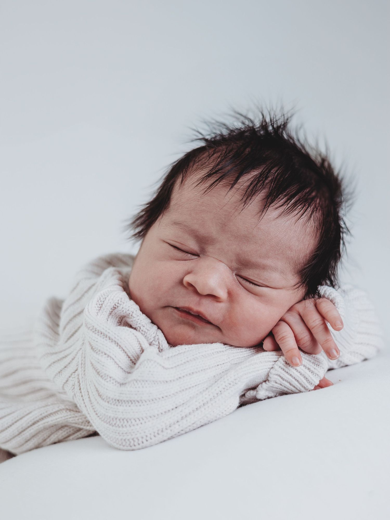 A sleeping newborn baby swaddled in white knit blanket shown from three different angles in a series of photos.