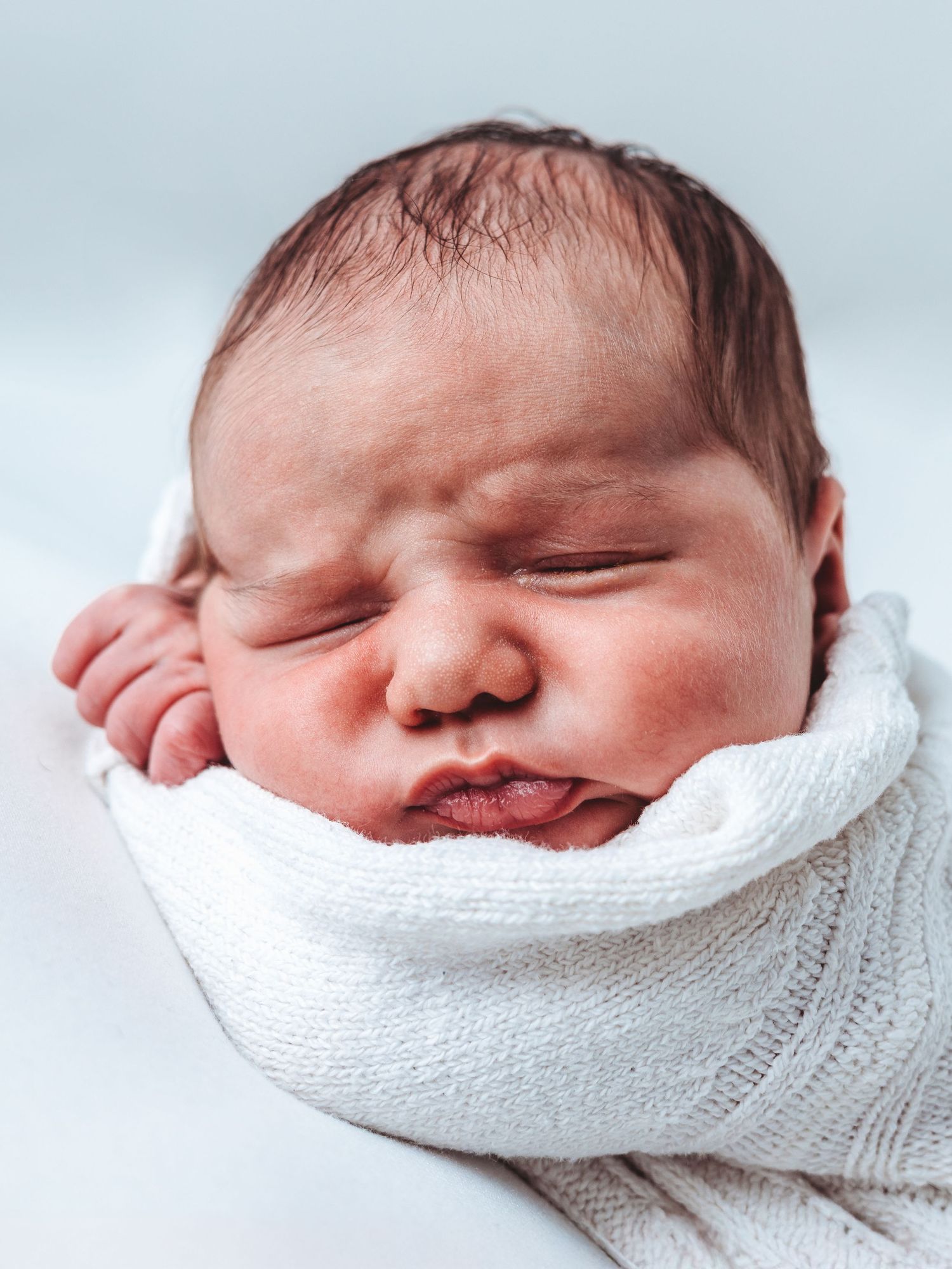 A sleeping newborn baby swaddled in white fabric shown from four different angles.