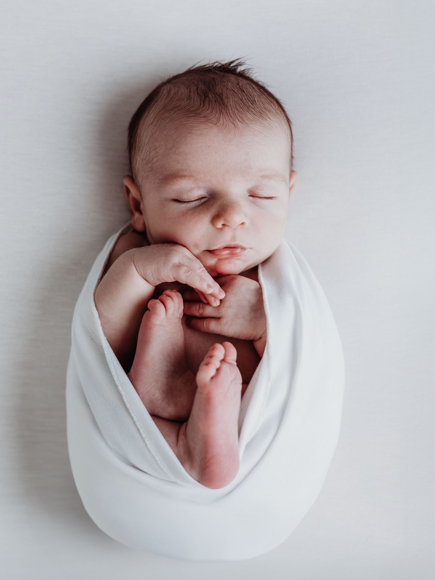 Newborn baby wrapped in white blanket shown from different angles against light background.