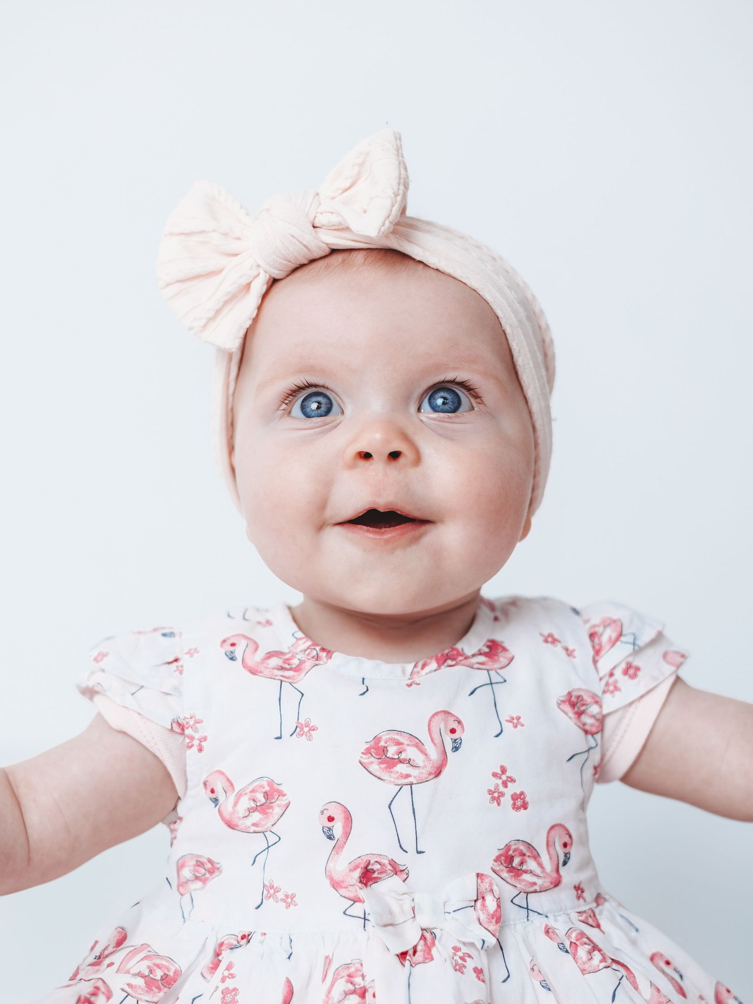Baby wearing white and pink floral dress with matching headband smiles in three different poses.