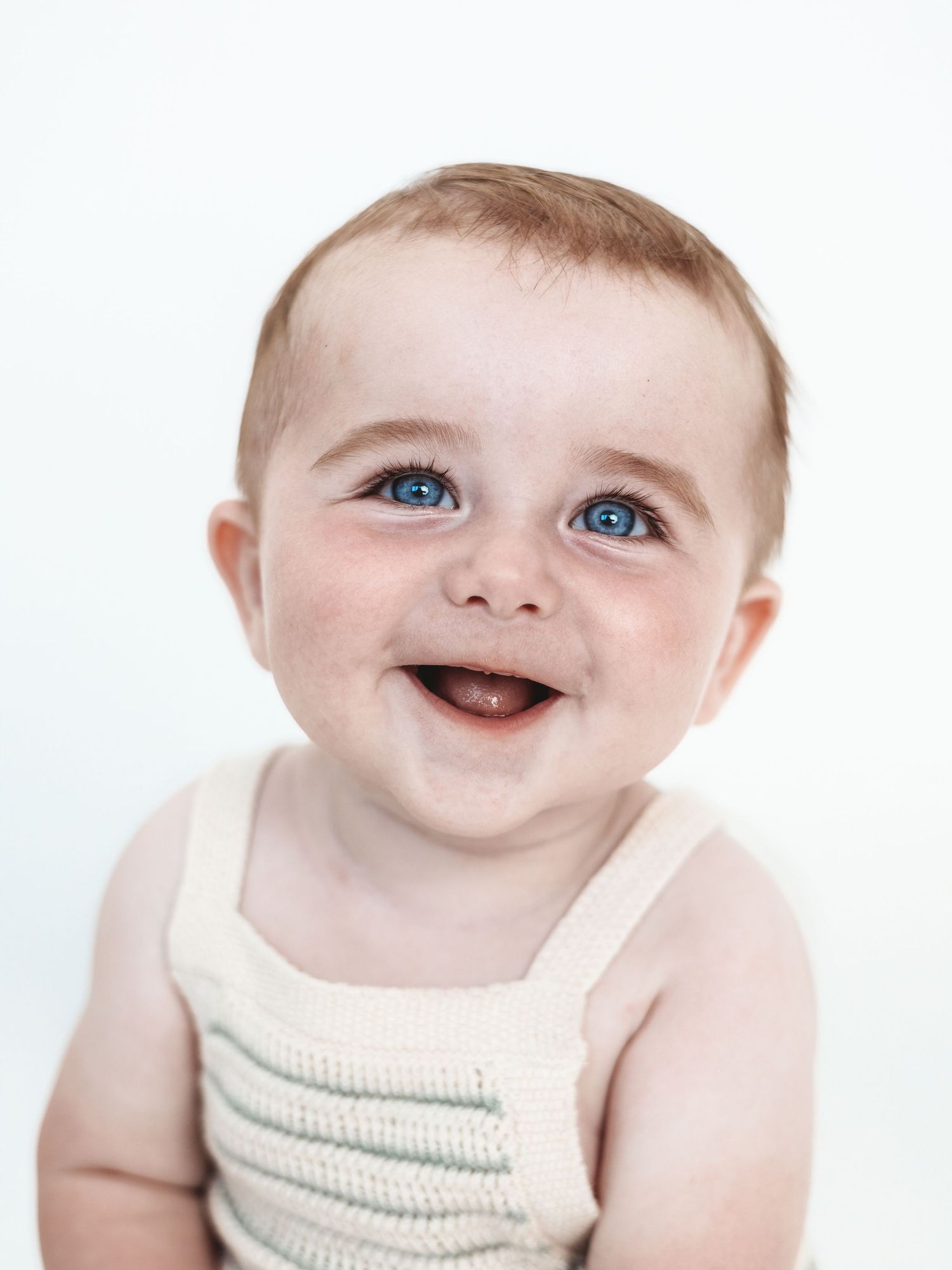 A smiling baby wearing a cream colored knit sweater showing joyful expressions in a series of photos.