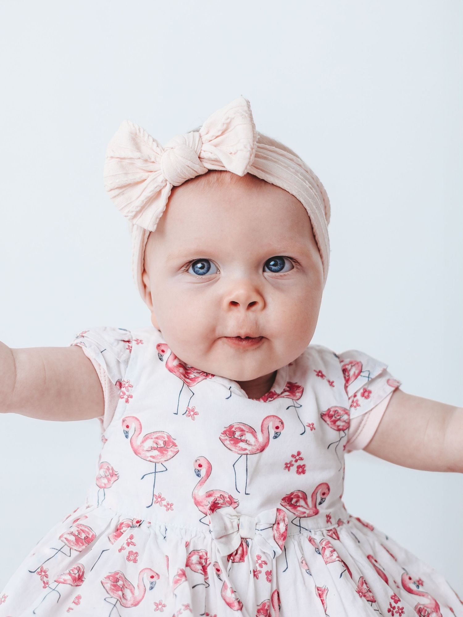 Baby wearing a pink floral dress and matching bow headband against a white background.