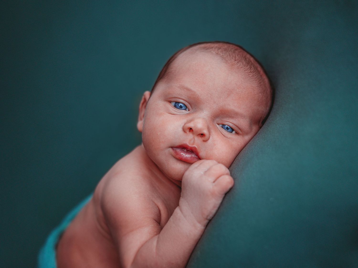 Series of seven photos showing a newborn baby against a teal background in various sleeping poses.