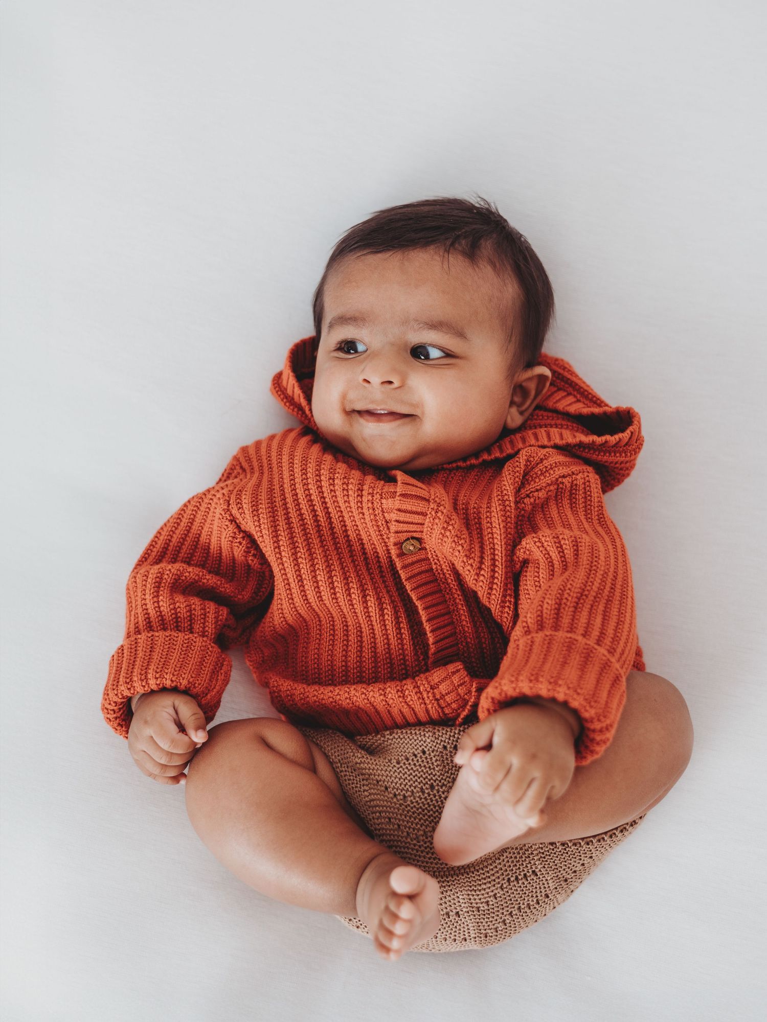 Baby wearing orange knit sweater and brown pants lying on white background in three different poses.