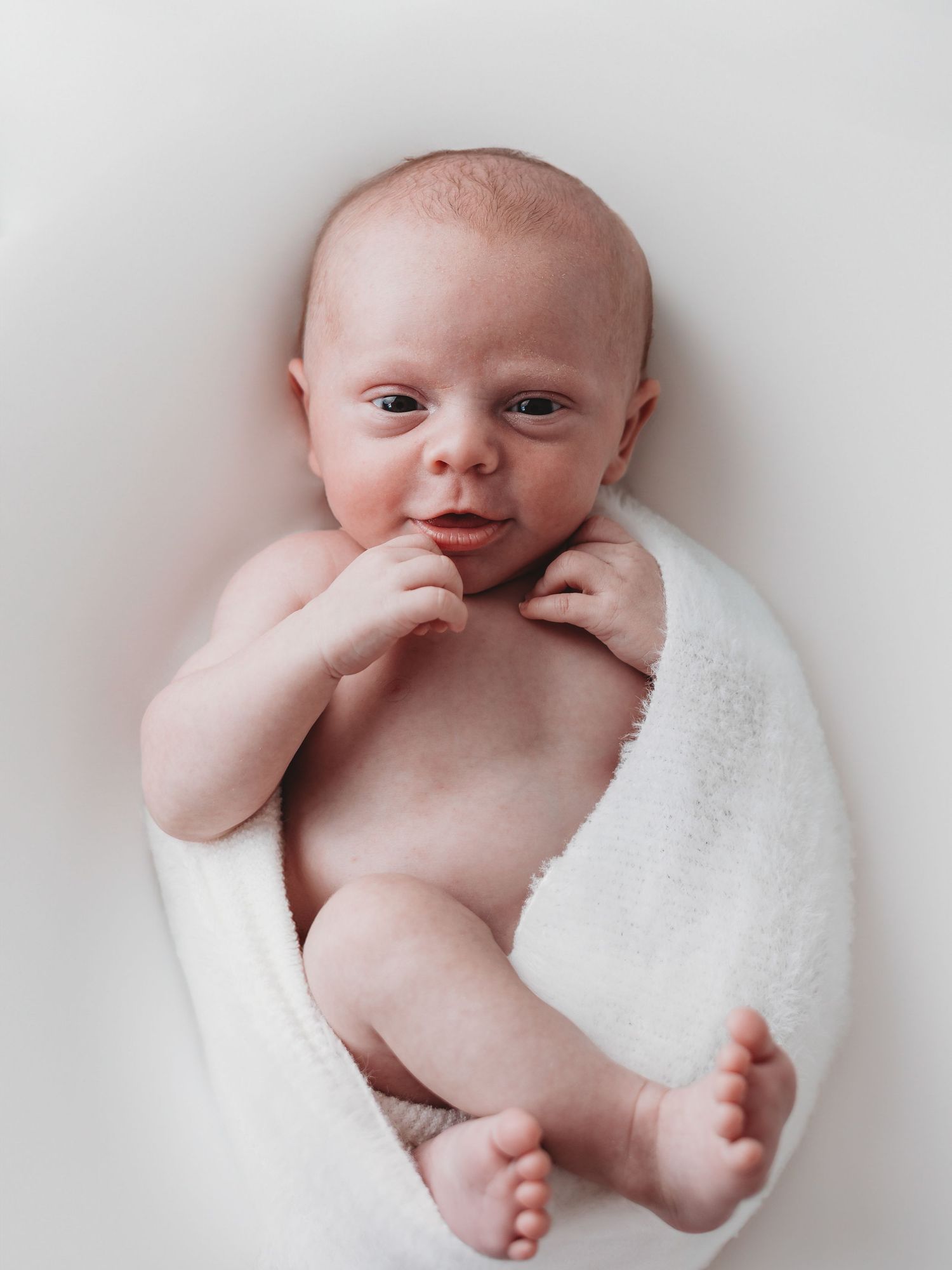 A series of black and white newborn photos showing a baby in various poses wrapped in soft white fabric against a light background.