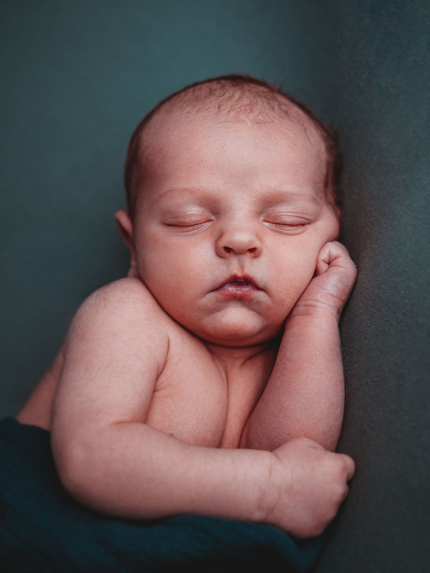 A sleeping newborn baby curled up peacefully in a fetal position against a dark background.