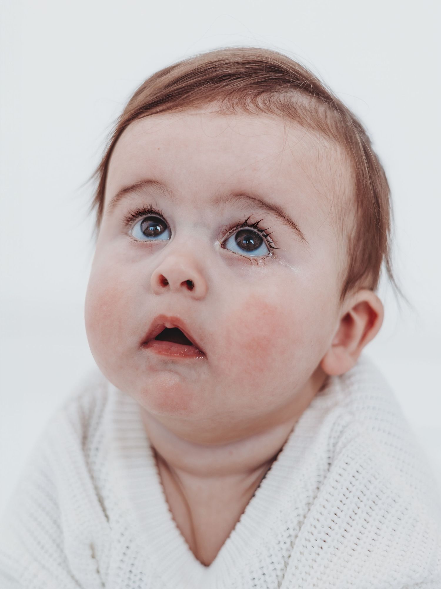 Baby in white knit sweater looking up with bright blue eyes and rosy cheeks in a series of candid expressions.