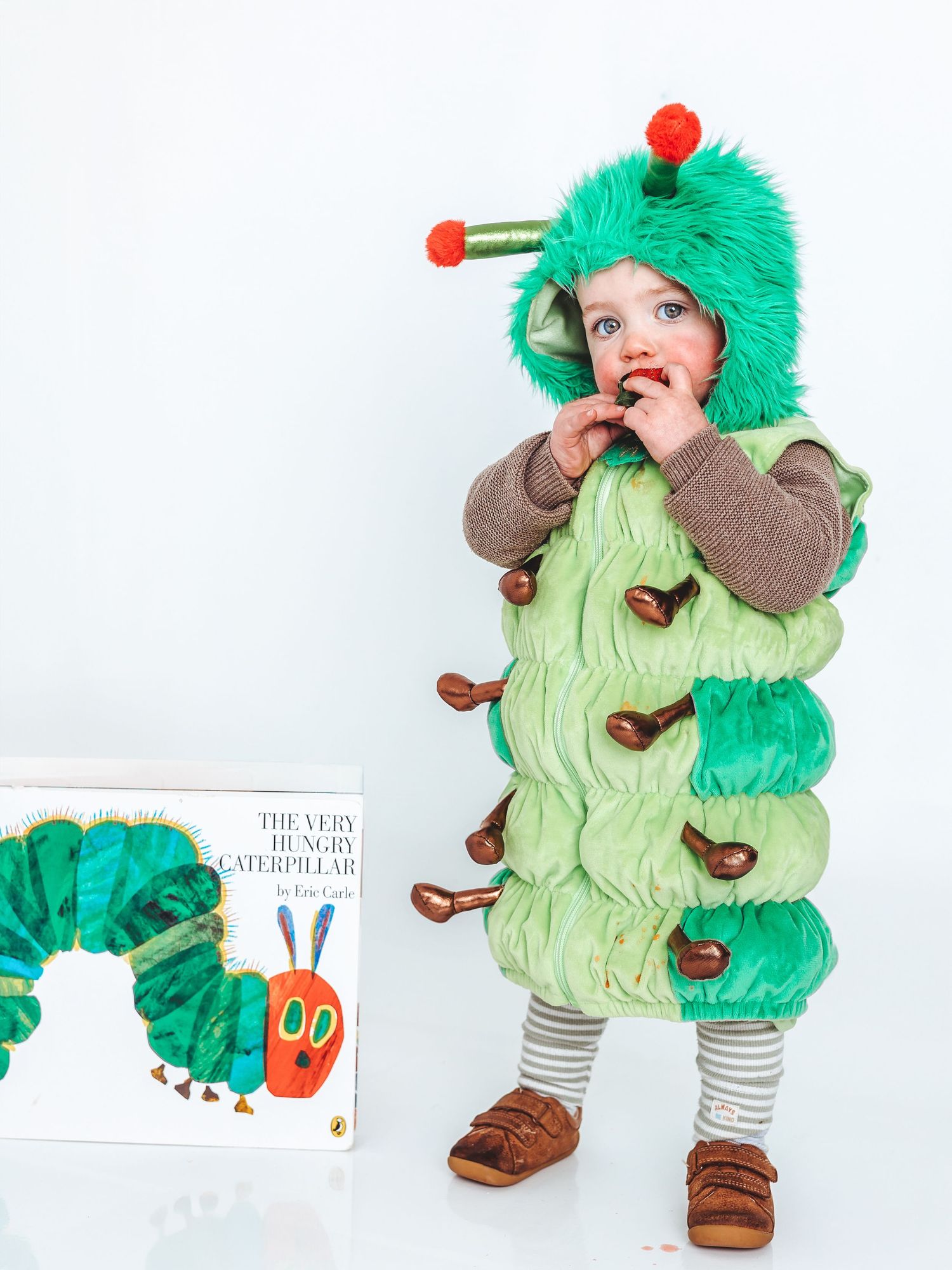 Toddler in Very Hungry Caterpillar costume poses next to the classic Eric Carle book.
