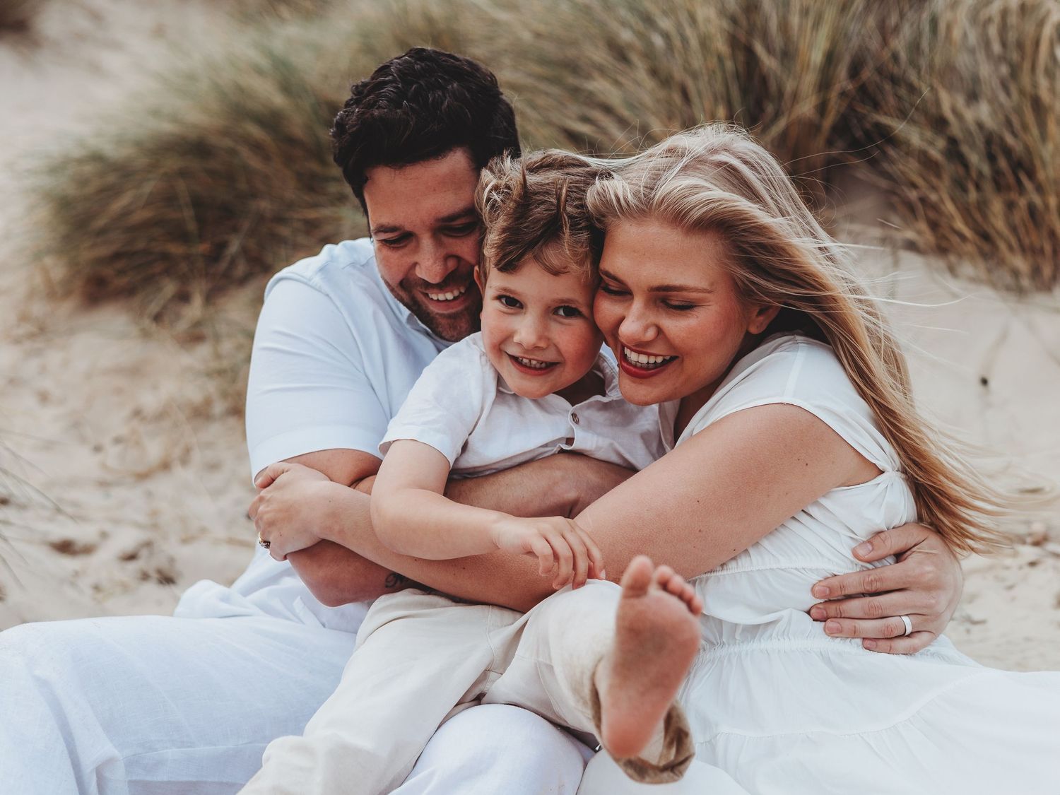 A couple embraces while lying on white sand during a romantic beach photoshoot.
